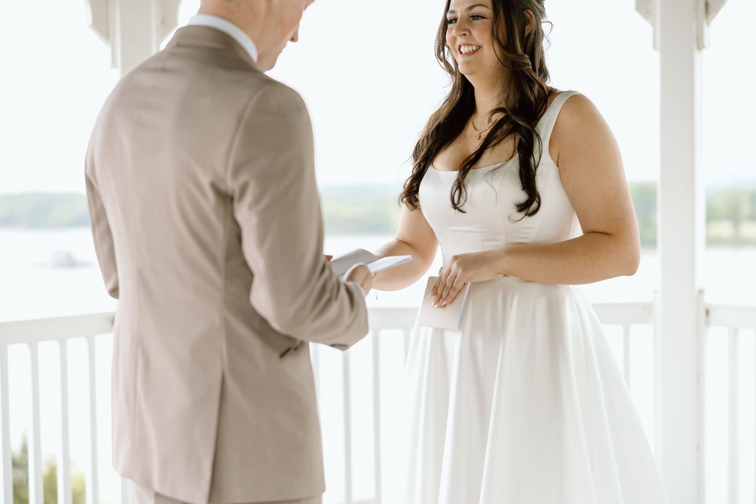 A couple in wedding attire share an intimate moment on a white porch during their special day.