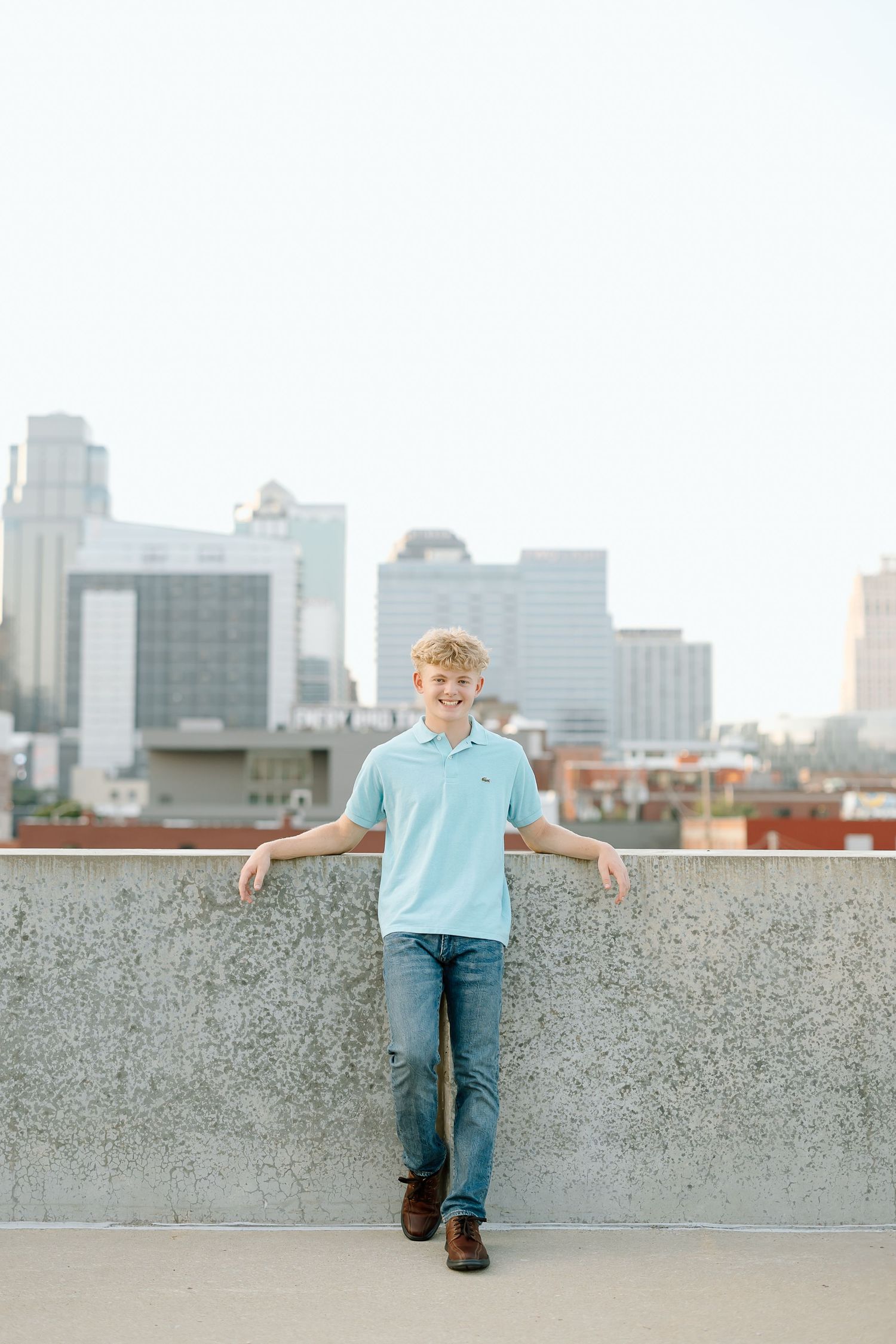 A person in a light blue shirt and jeans sits on a concrete wall with a city skyline in the background.