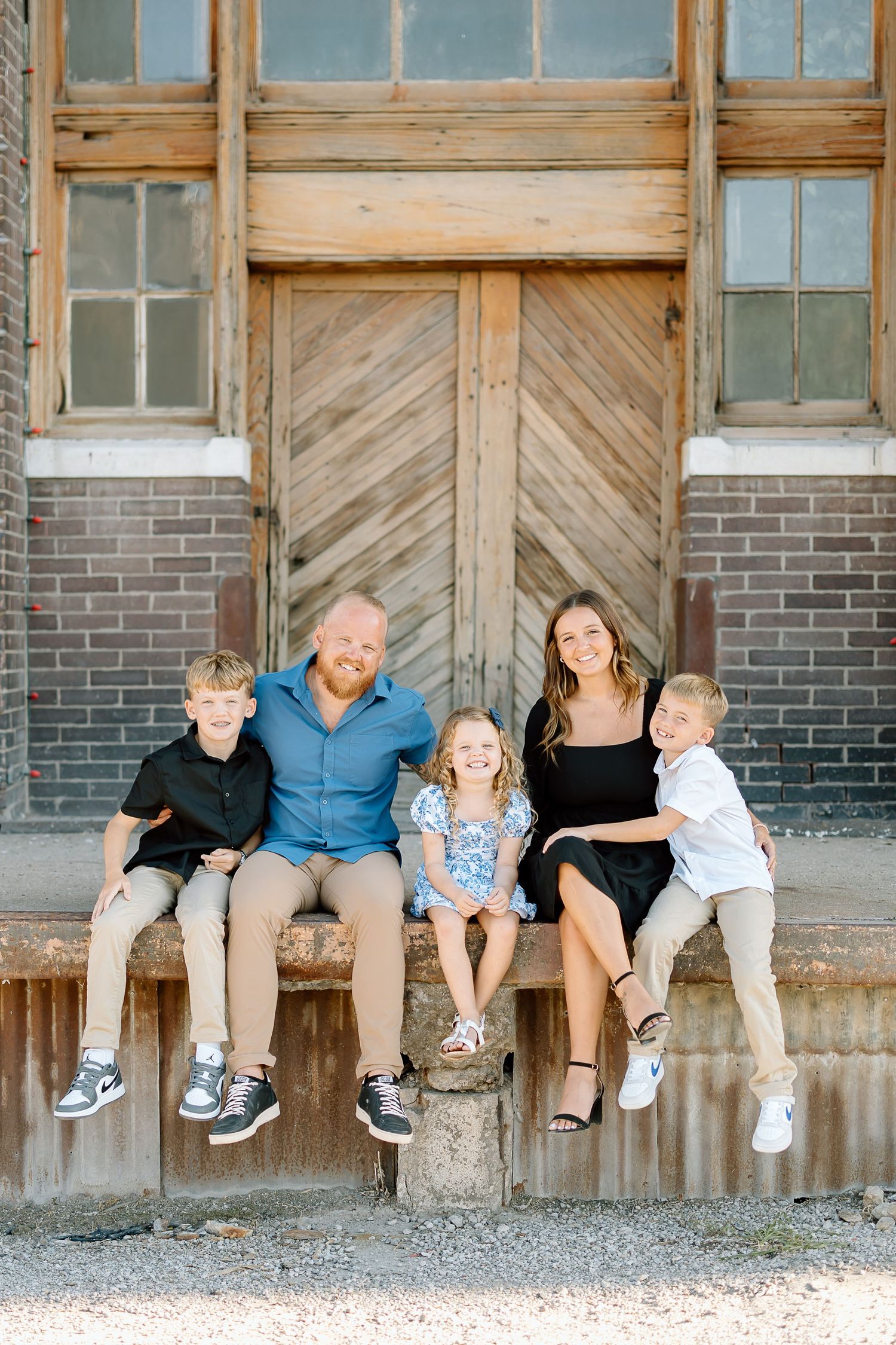 A family sits together on a rustic wooden step in front of a vintage door with brick and glass panels.