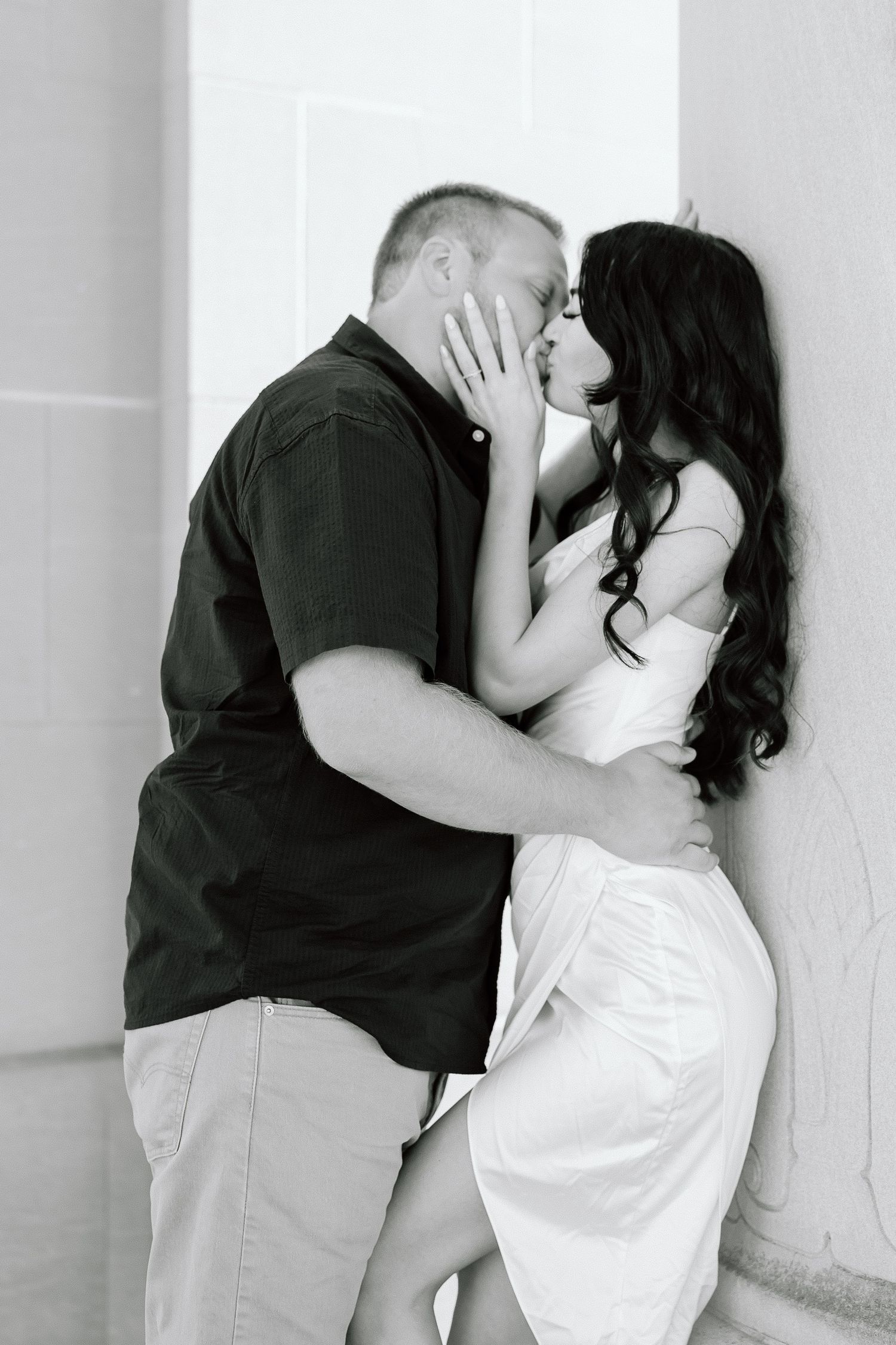 A romantic black and white photo of a couple sharing an intimate kiss against a white wall.