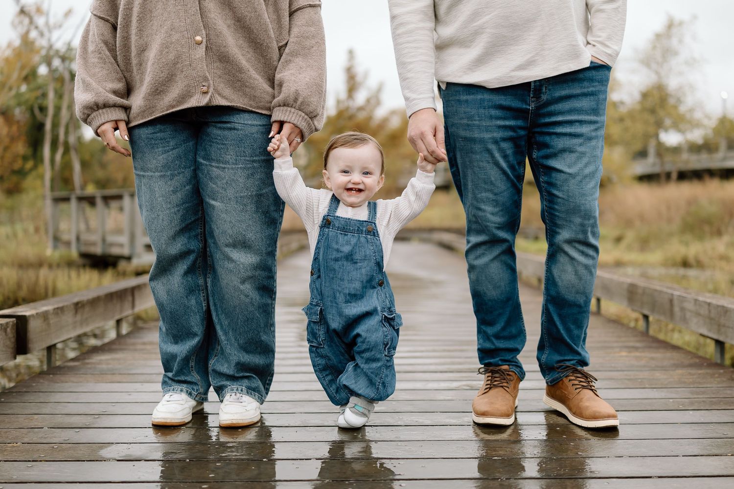 Three pairs of legs standing on a wooden boardwalk, with the middle wearing adorable blue denim overalls.