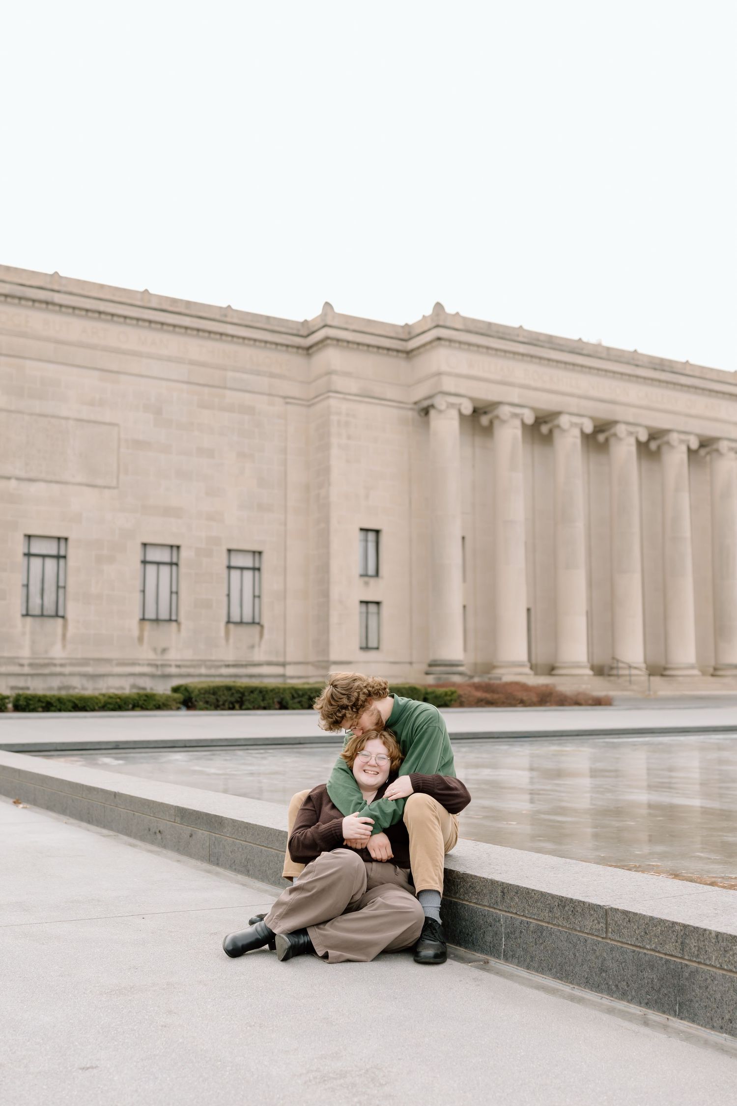 A couple shares a romantic moment while sitting on stone steps outside a grand neoclassical building.