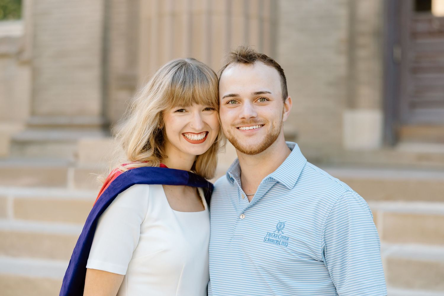 A couple shares a joyful moment together on stone steps while wearing light colored casual clothing.
