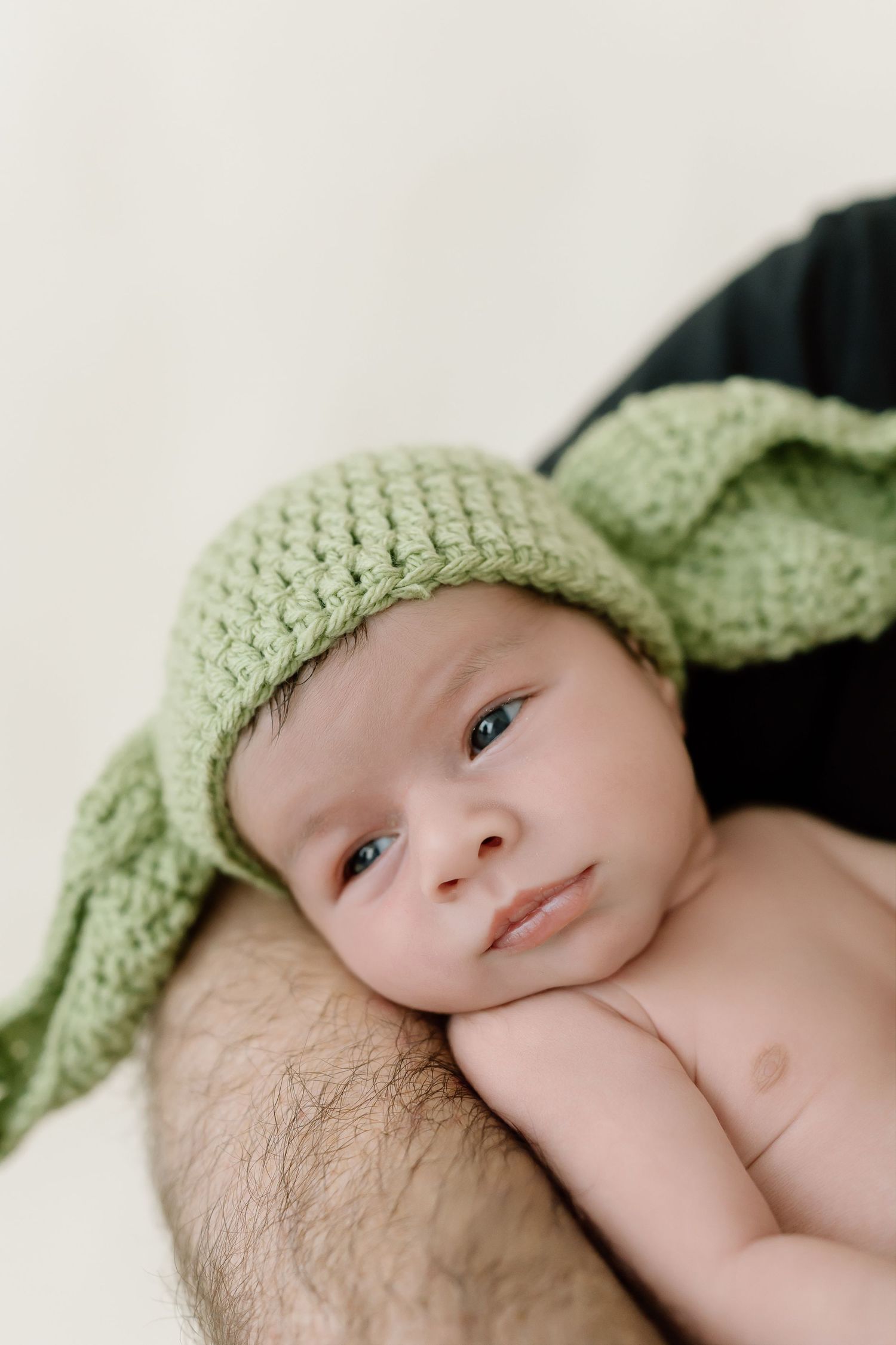 Baby wearing a soft mint green knitted hat lies peacefully against white bedding.