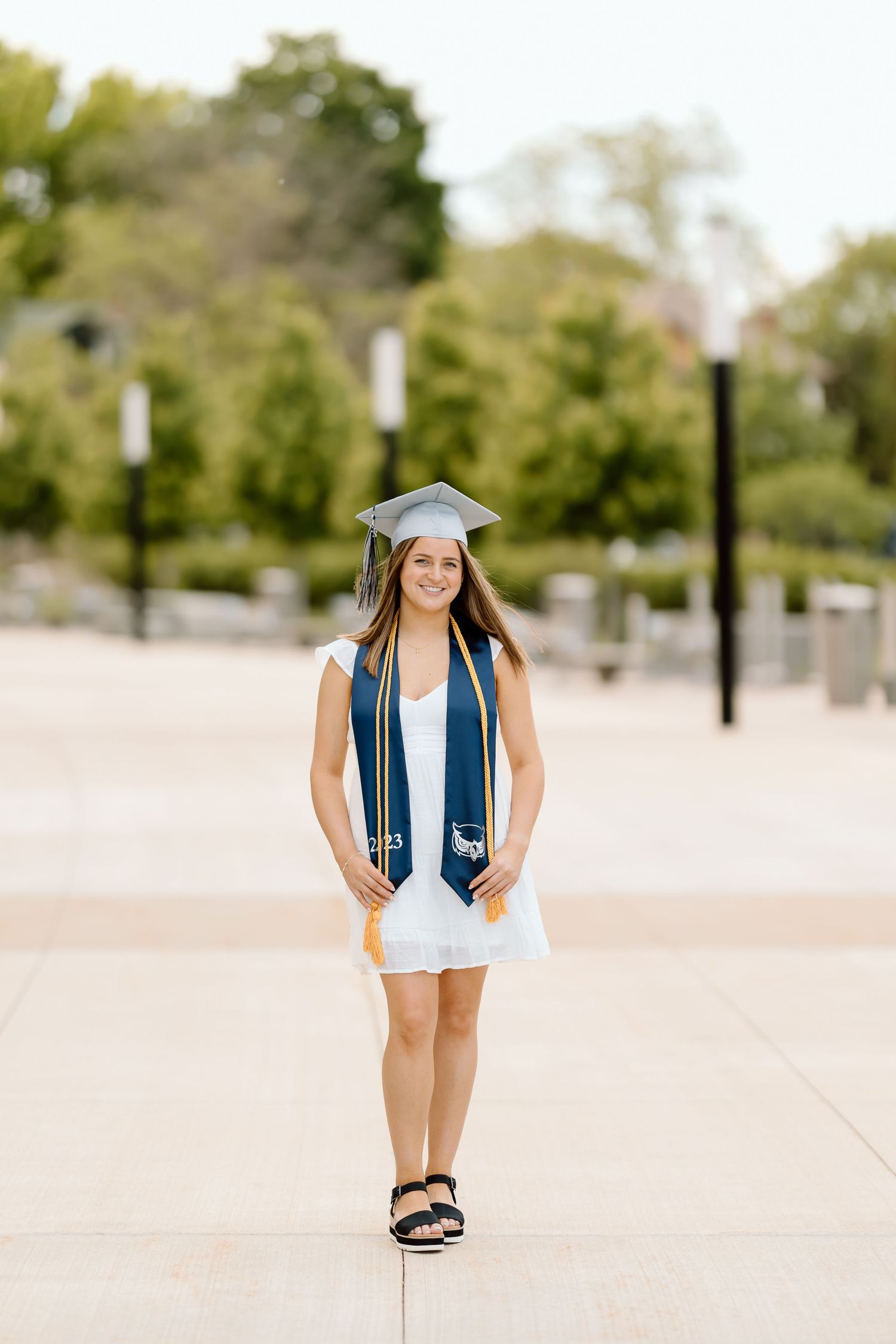 A graduate in cap and gown poses playfully in a series of four outdoor photos on a sunny day.