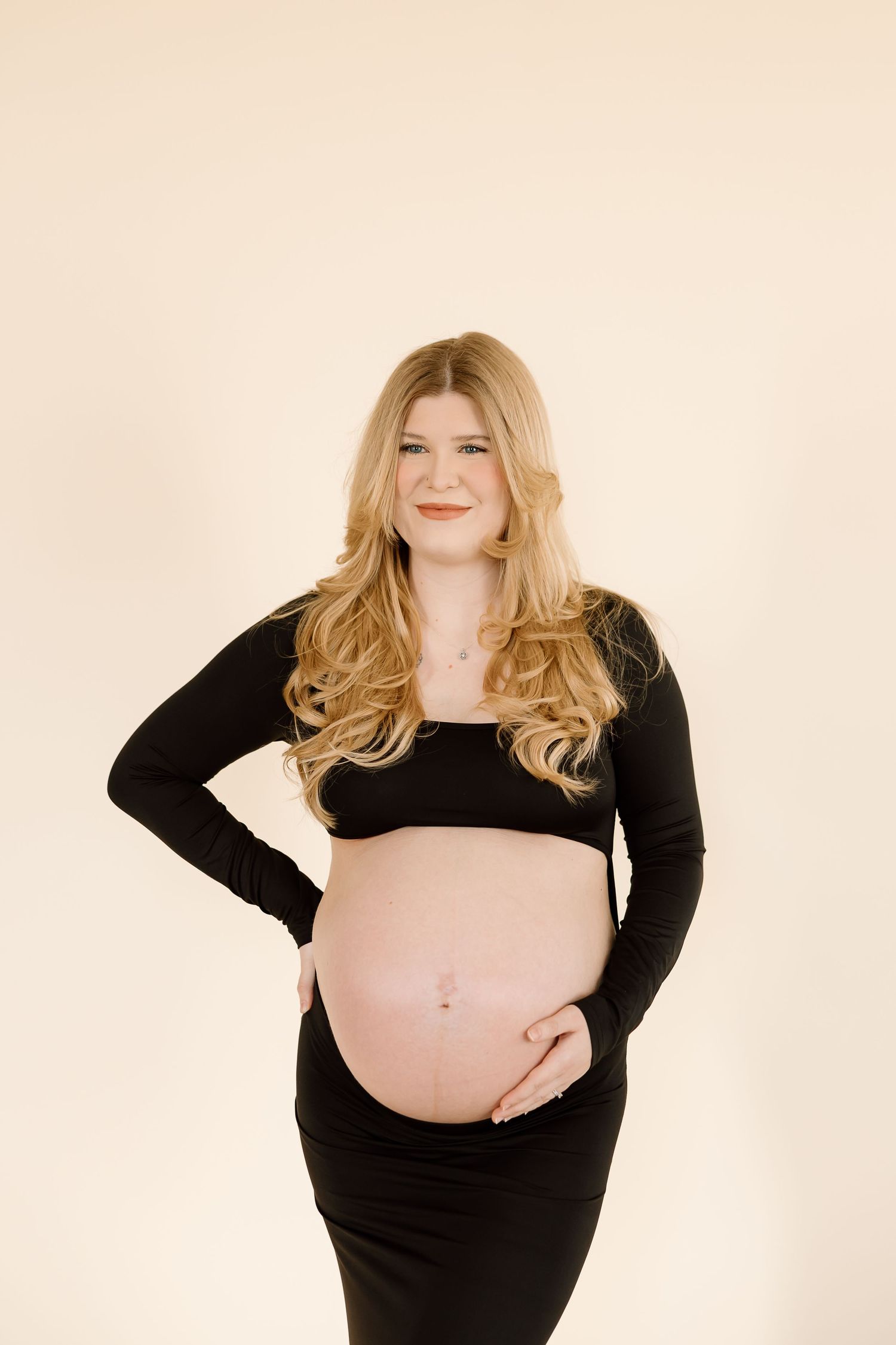 Contemporary maternity portrait featuring black two-piece outfit against neutral backdrop.