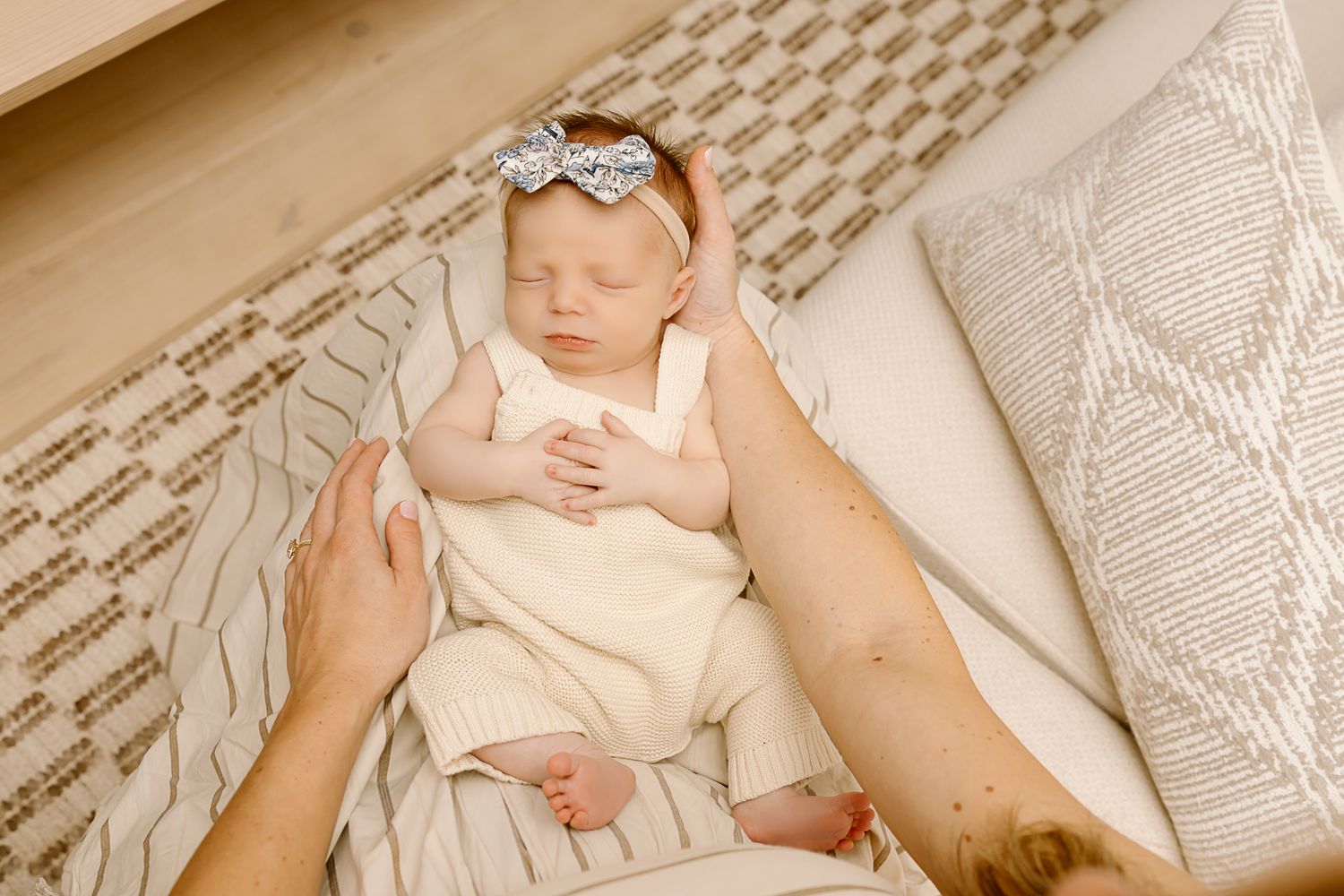 Infant wearing a white dress and bow headband lying on patterned bedding.