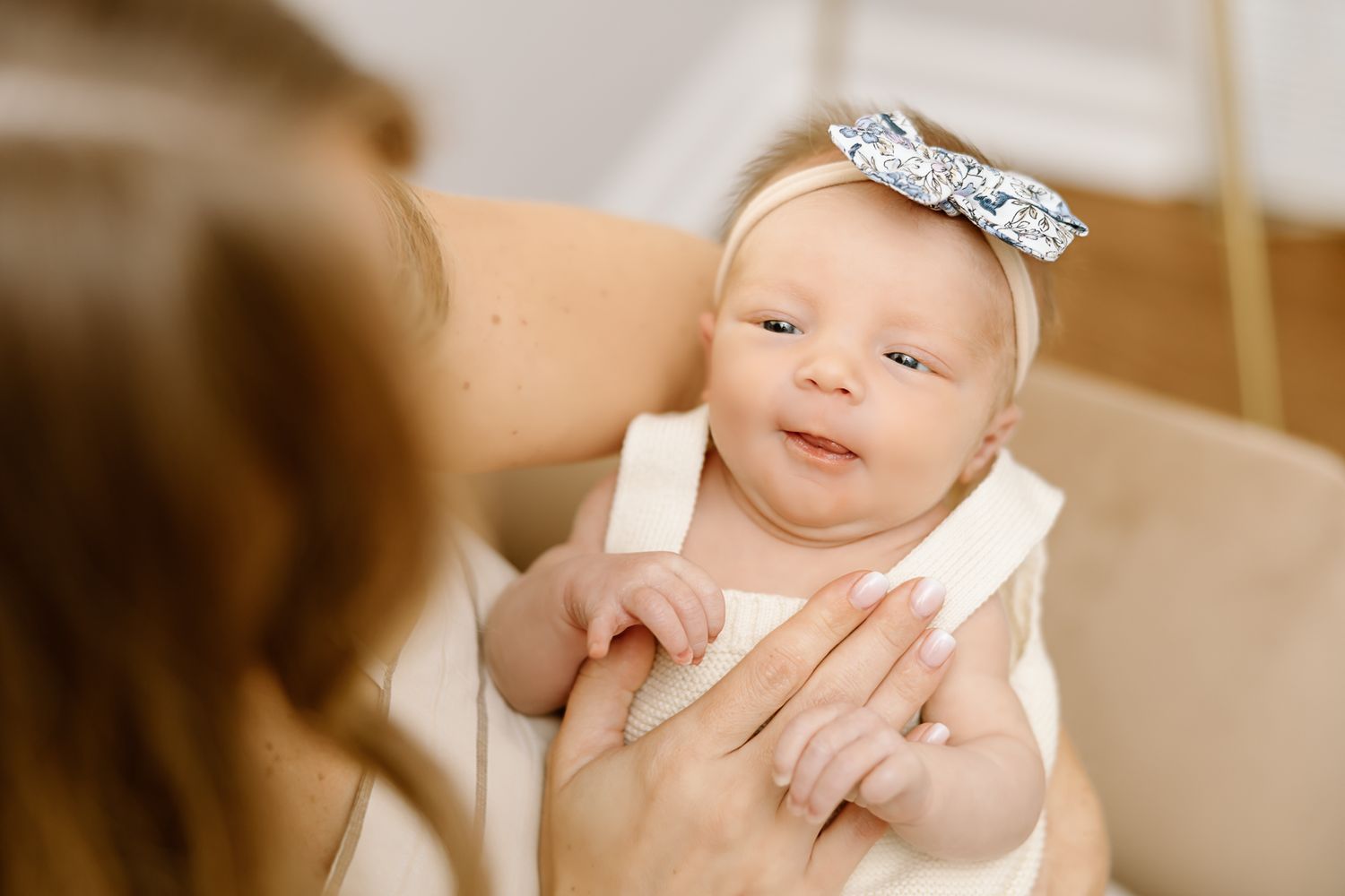Baby wearing white outfit and sparkly bow headband resting in caregiver's arms.
