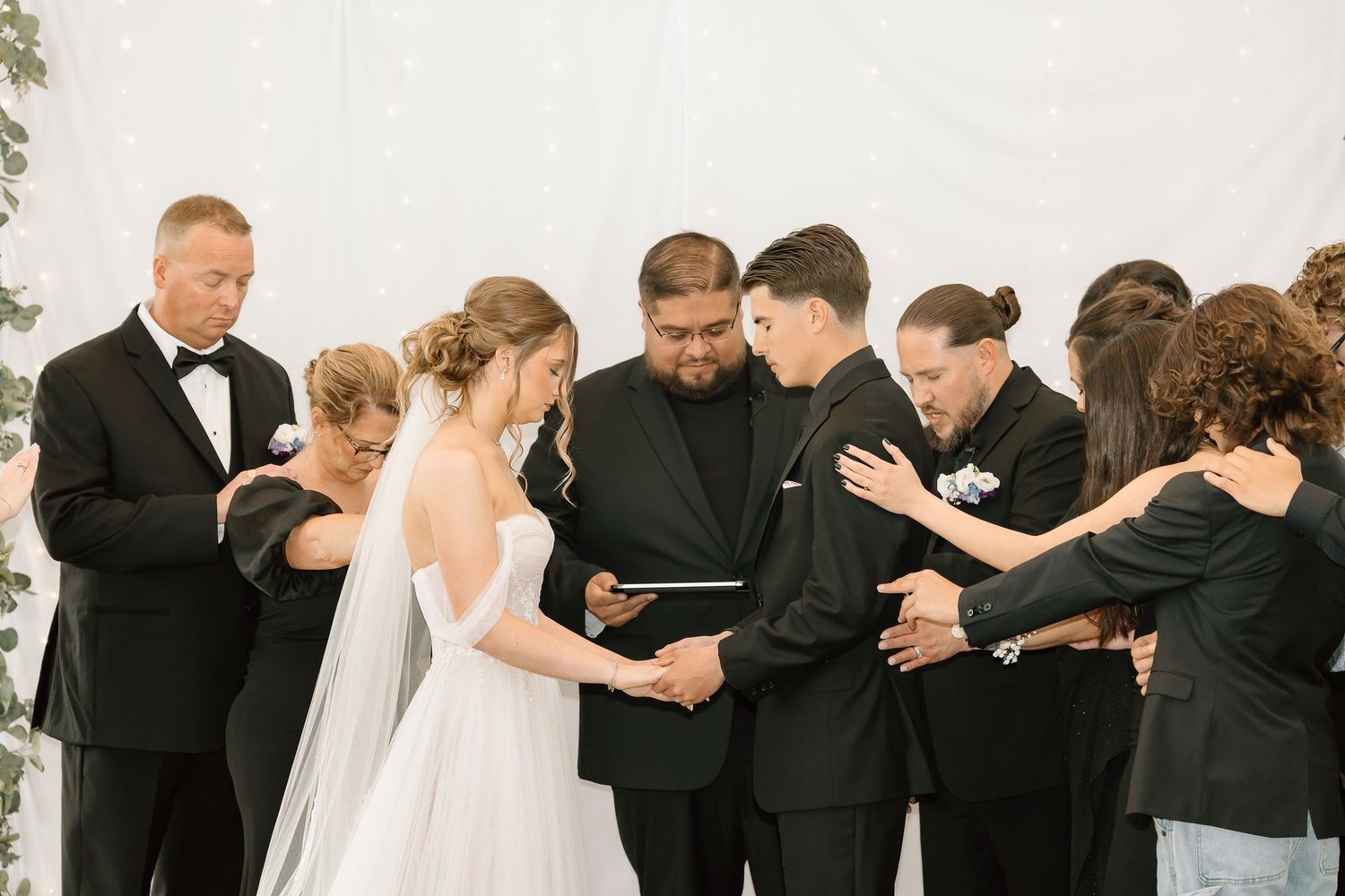 Wedding ceremony prayer moment with guests gathered around couple.