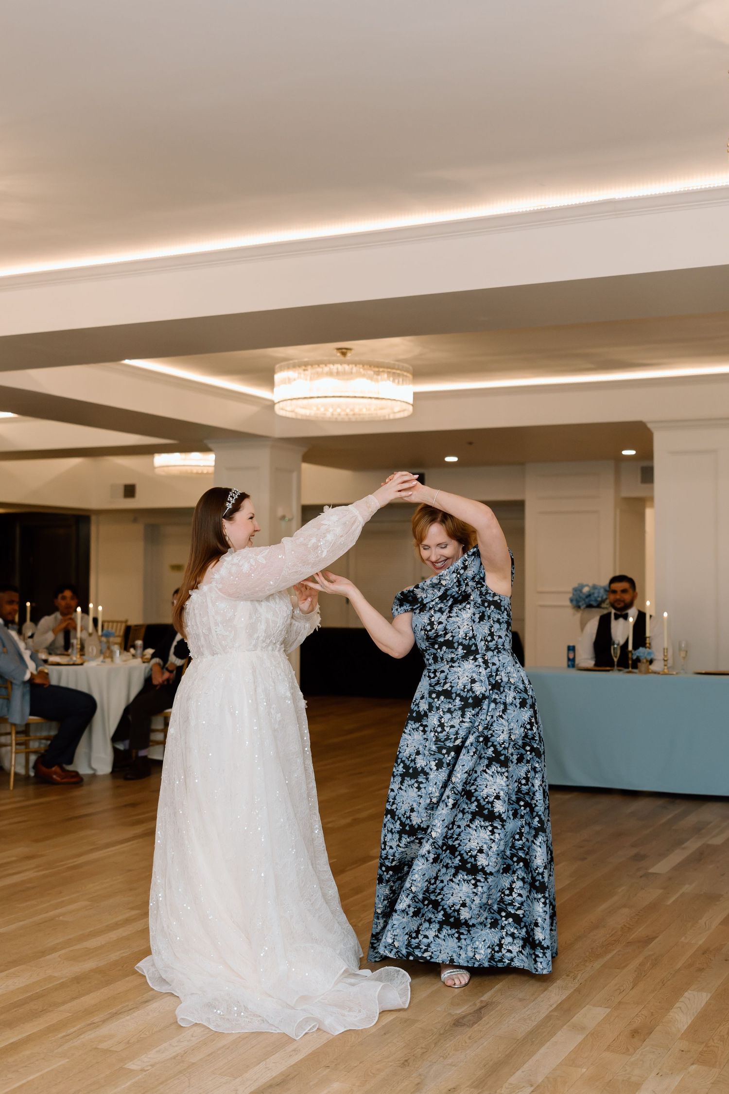 Bride in white gown dancing with guest in floral dress at elegant wedding reception venue.