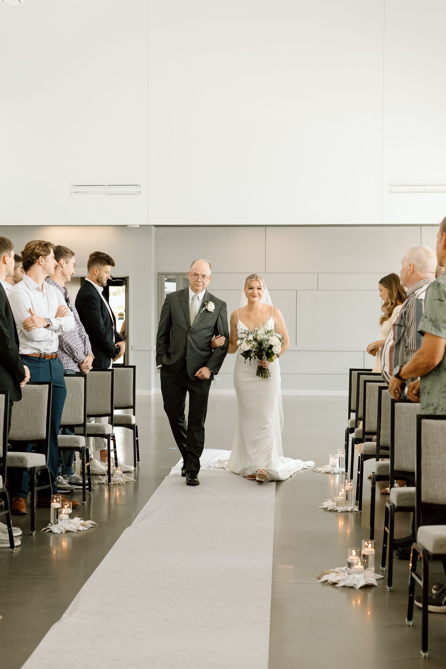Wedding aisle decorated with modern minimalist aesthetic in white and black tones and glowing candles along the sides.