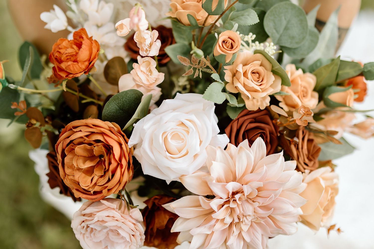 Elegant floral arrangement with peach roses, pink dahlias, and eucalyptus greenery in soft romantic tones.