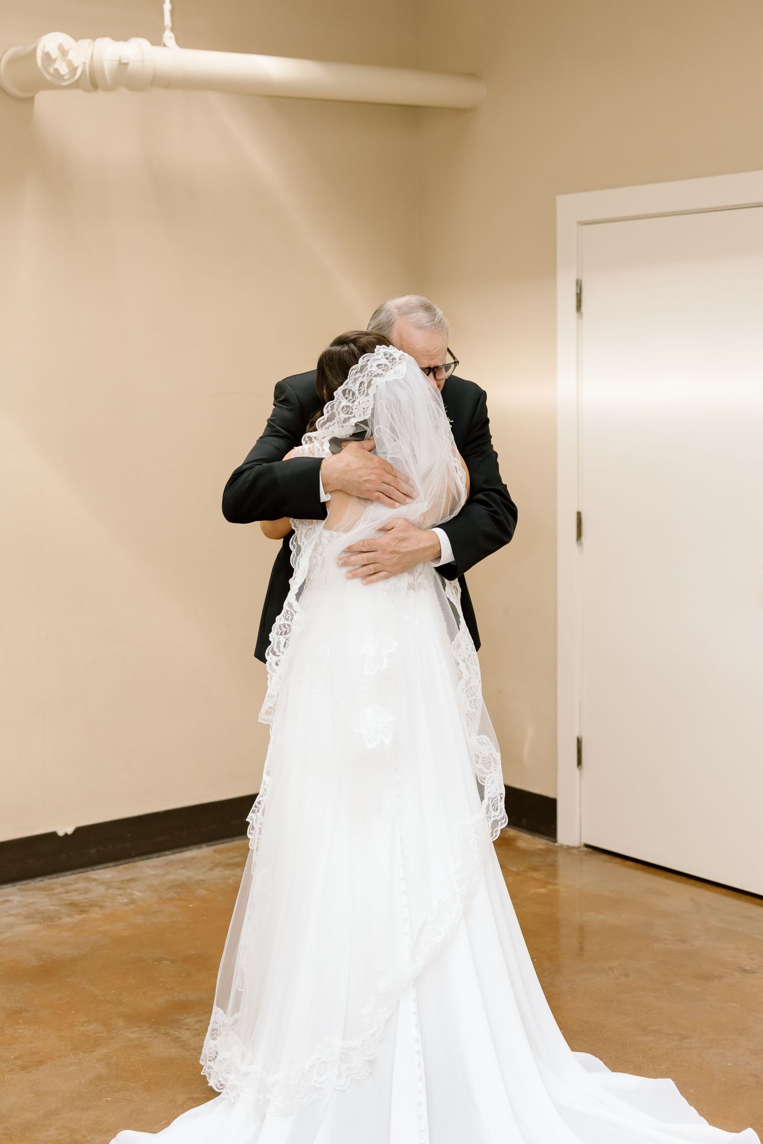 A tender embrace between two people in formal wedding attire, with a flowing white wedding dress visible.