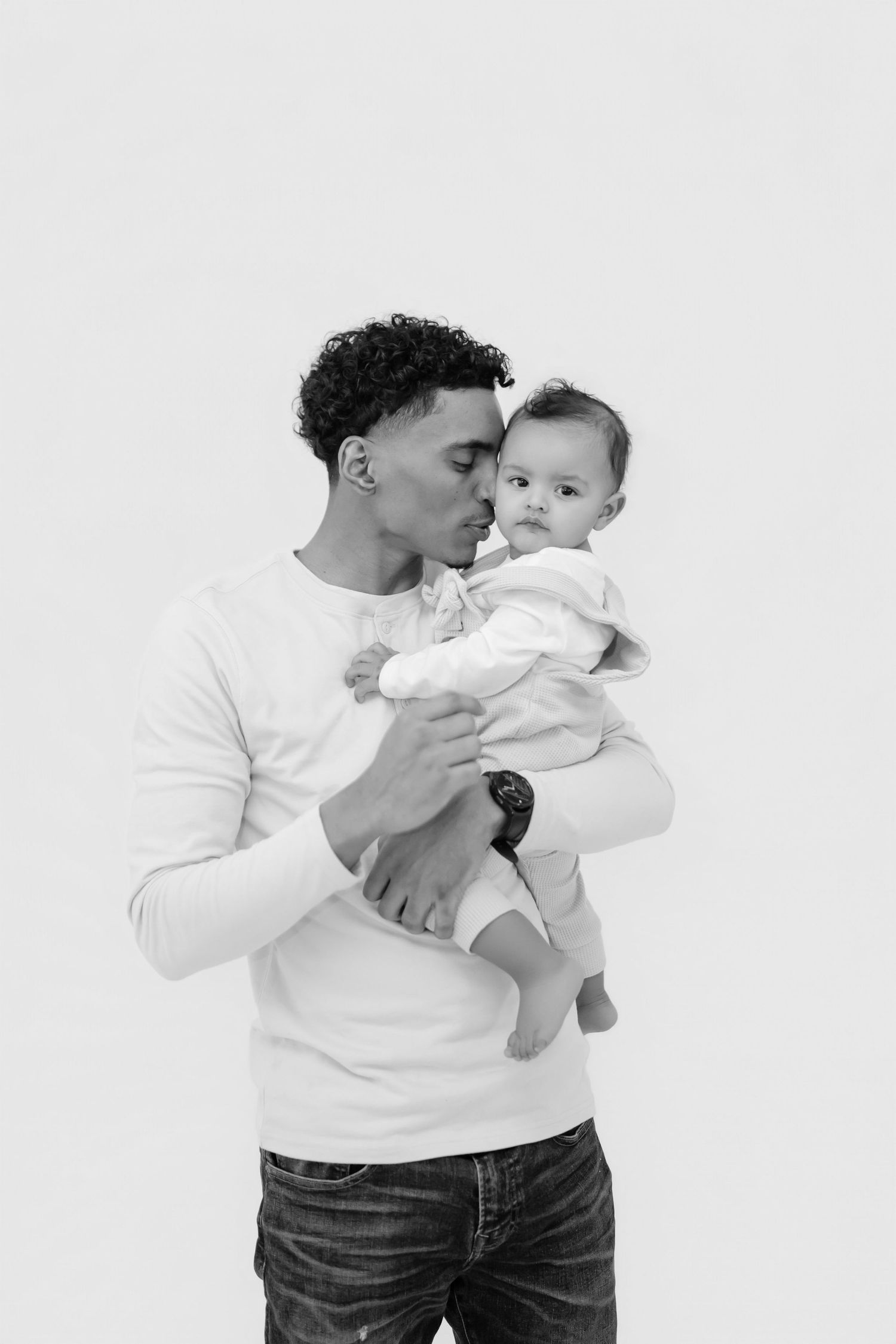 A tender moment captured in black and white as parent and baby interact in matching white tops against a light background.