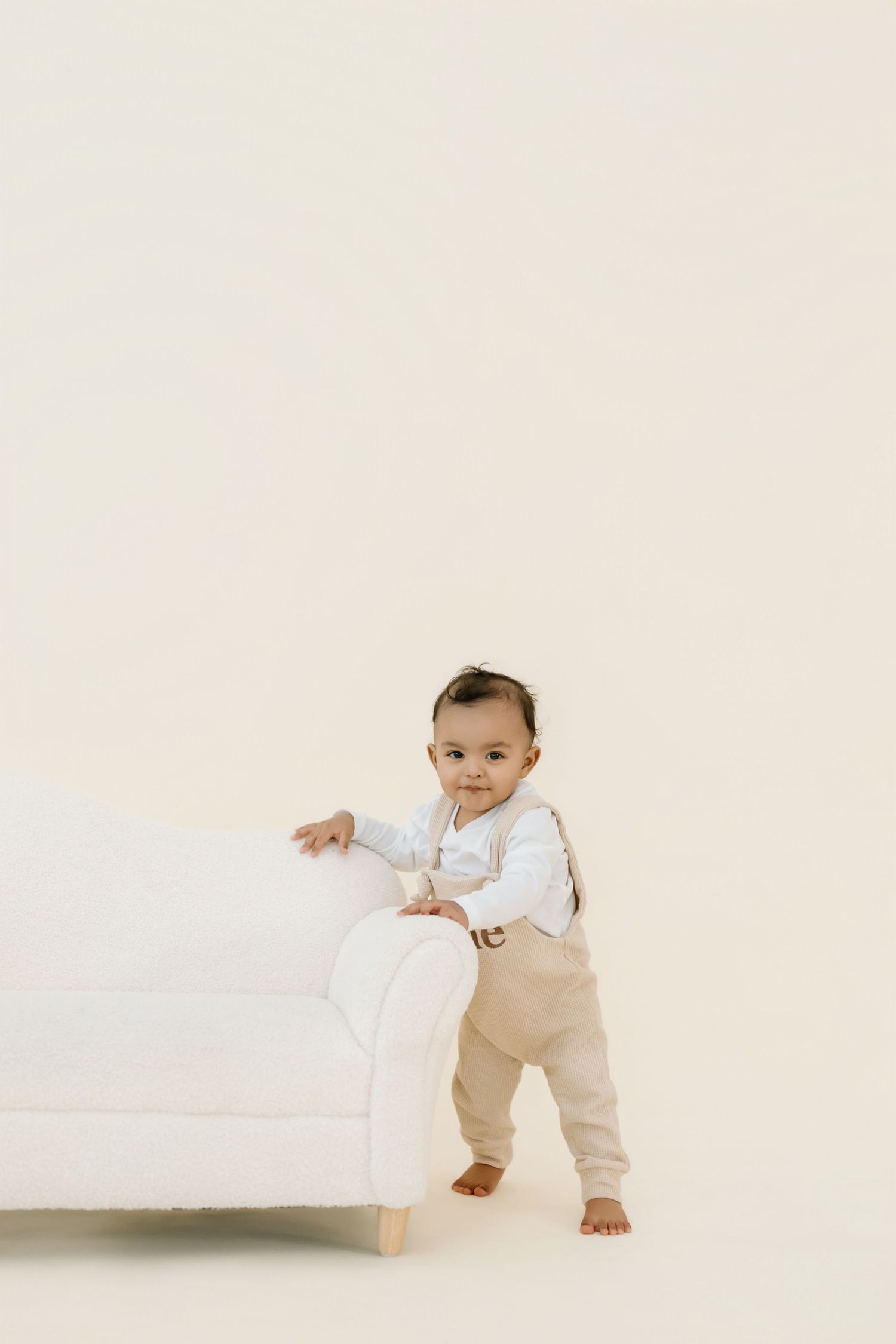 Baby in white and beige outfit crawling on white background.