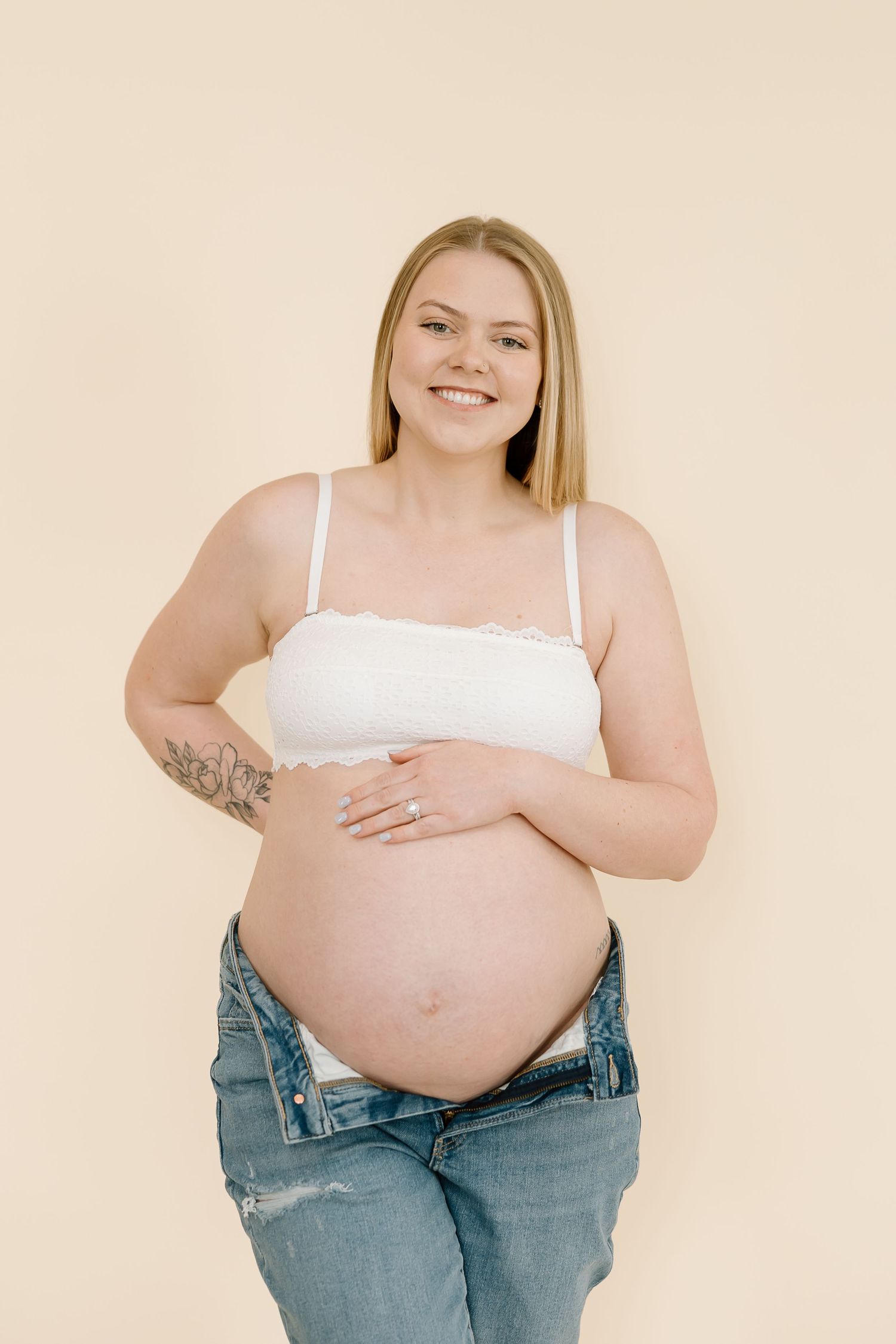 Radiant mother-to-be smiles while cradling baby bump in casual maternity portrait.