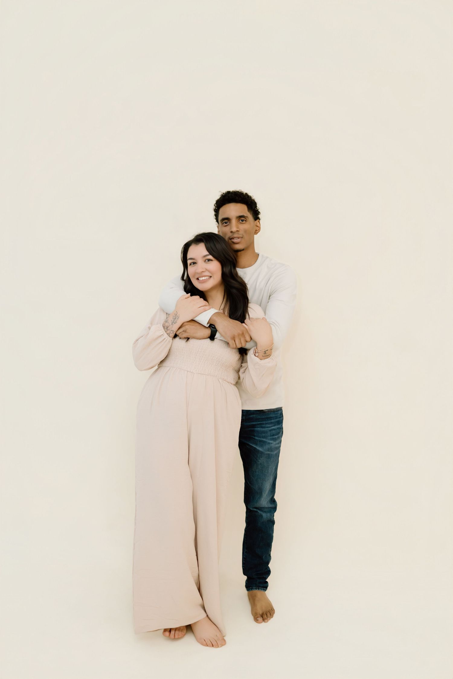 A couple embraces in a minimalist studio setting wearing casual attire against a white background.