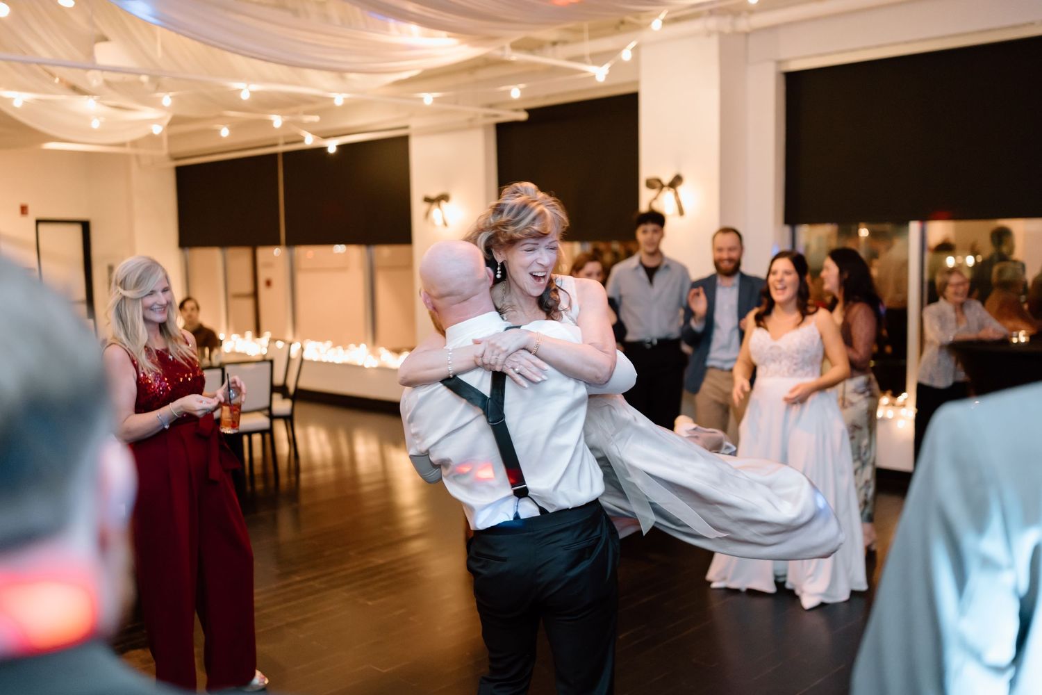 Panoramic view of an elegant ballroom wedding reception with white drapes and guests dancing on the dance floor.
