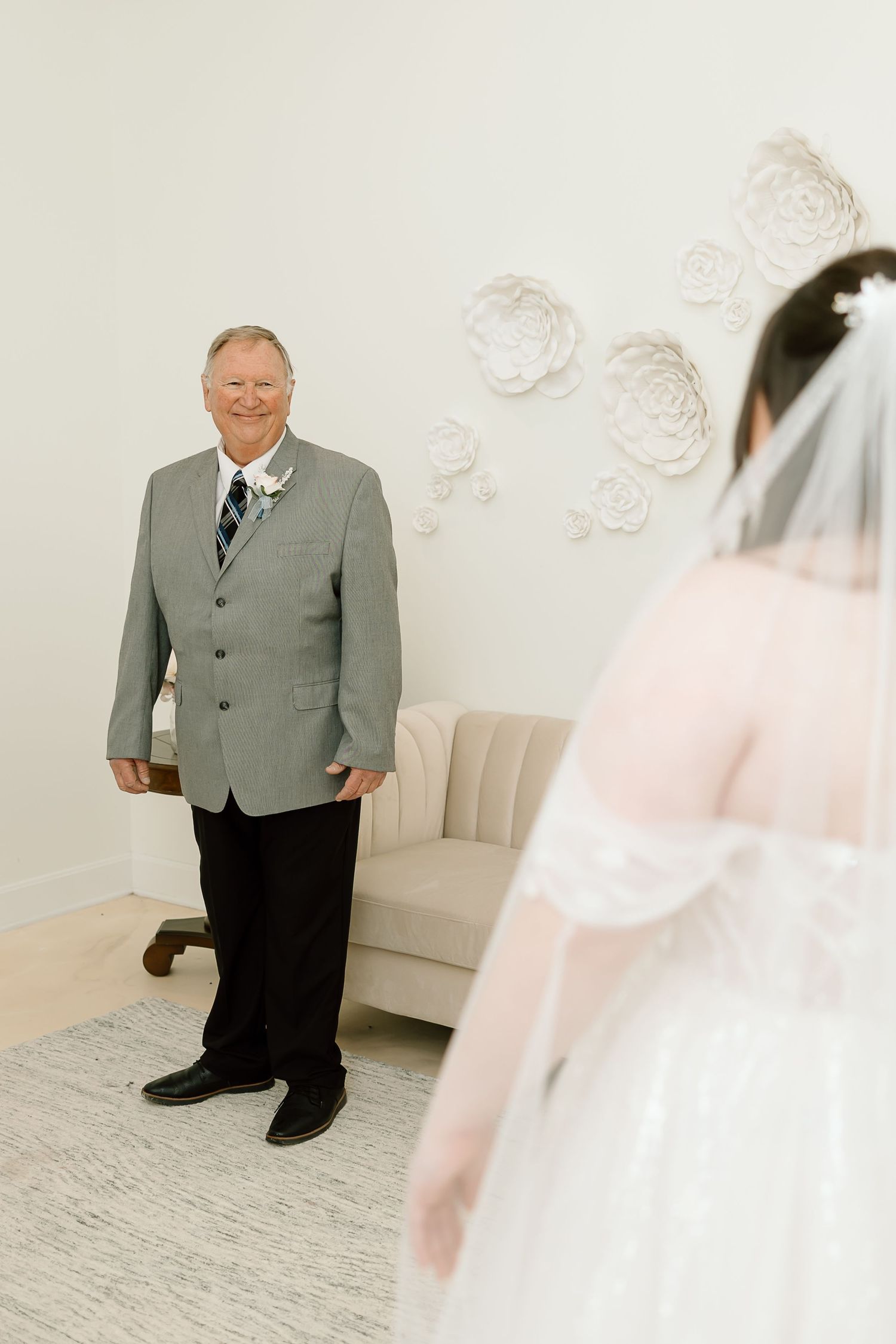 A tender wedding moment in a bright room with white floral wall decor and a gray sofa.