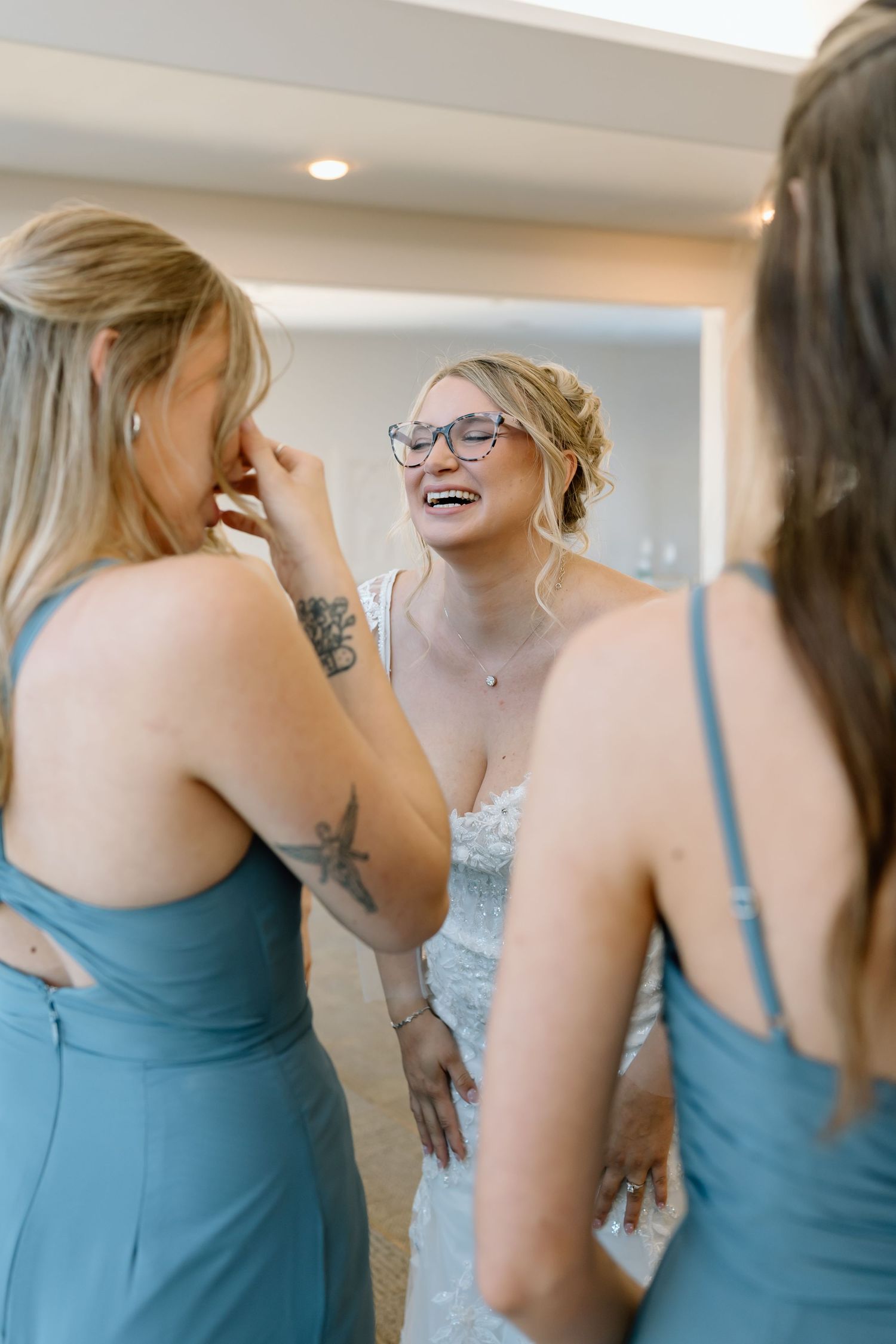 A group of bridesmaids in light blue dresses share an emotional moment while getting ready for a wedding.