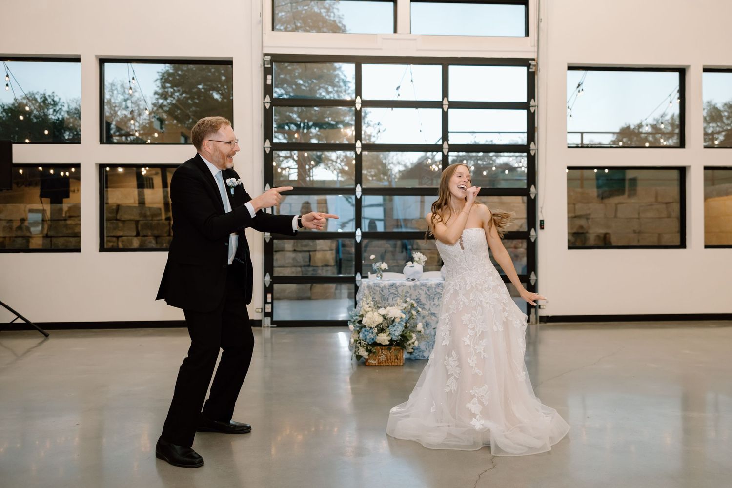 Bride and groom share their first dance in an elegant wedding reception venue with large windows.