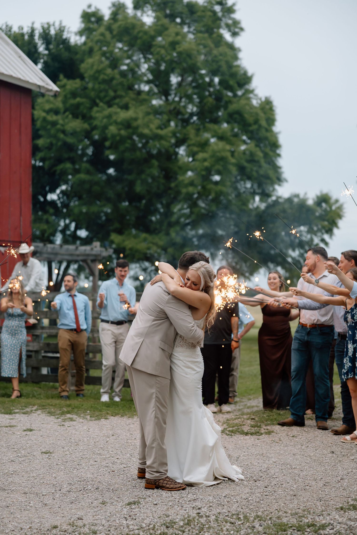 Newlywed couple embracing during sparkler send-off at rustic barn wedding celebration with guests.