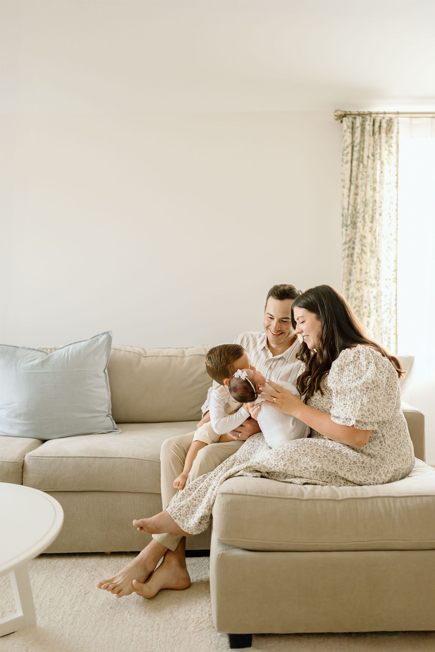 A parent and child share tender moments together while relaxing on a beige couch in a bright, airy living room.