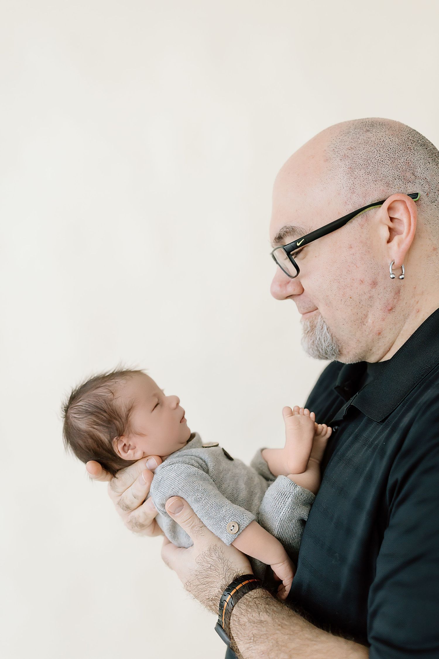 A person in black holds and gazes lovingly at a sleeping baby in a series of tender moments against a white background.