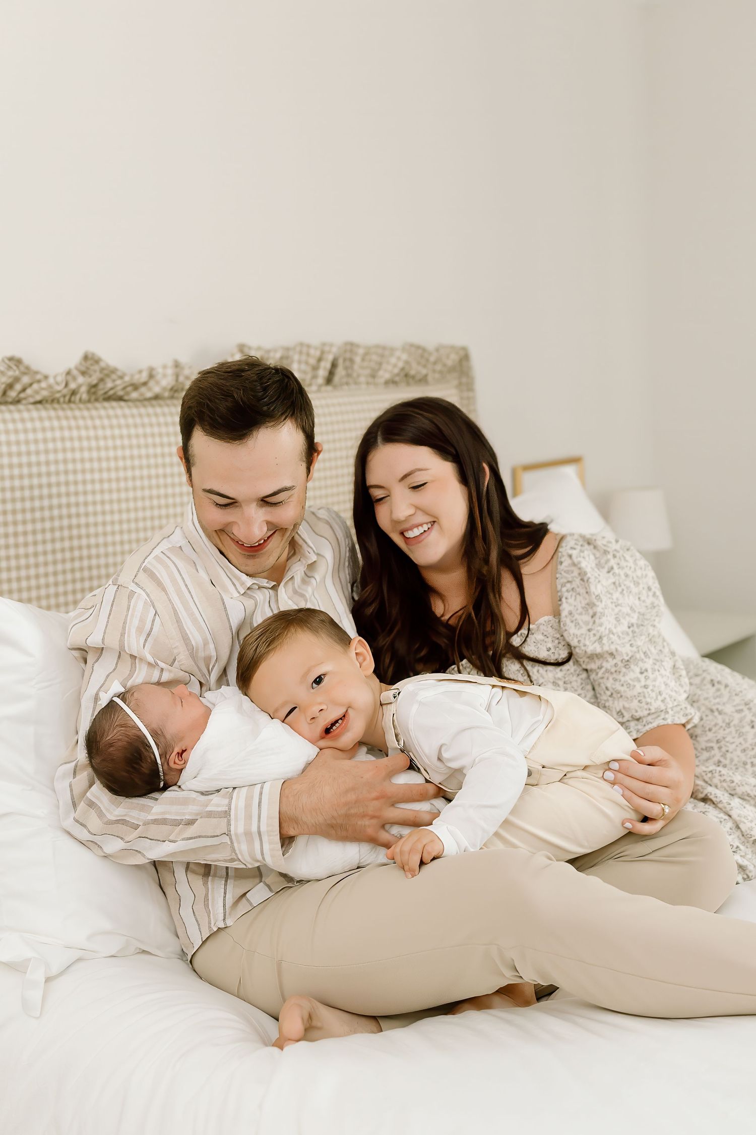 A family lies together on a white bed wearing matching cream colored loungewear in a cozy, intimate setting.