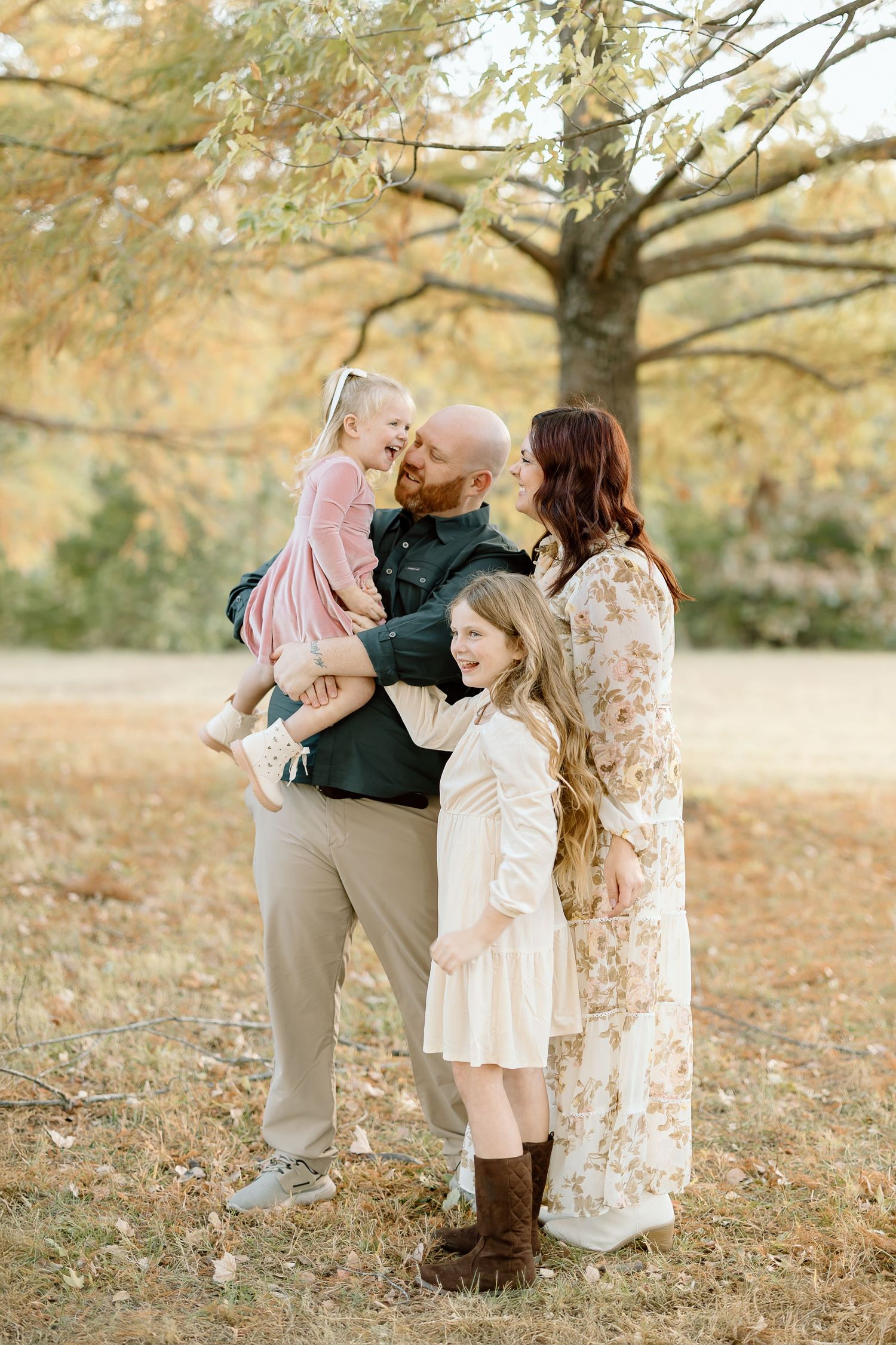A family shares tender moments together under autumn trees with fallen leaves on the ground.