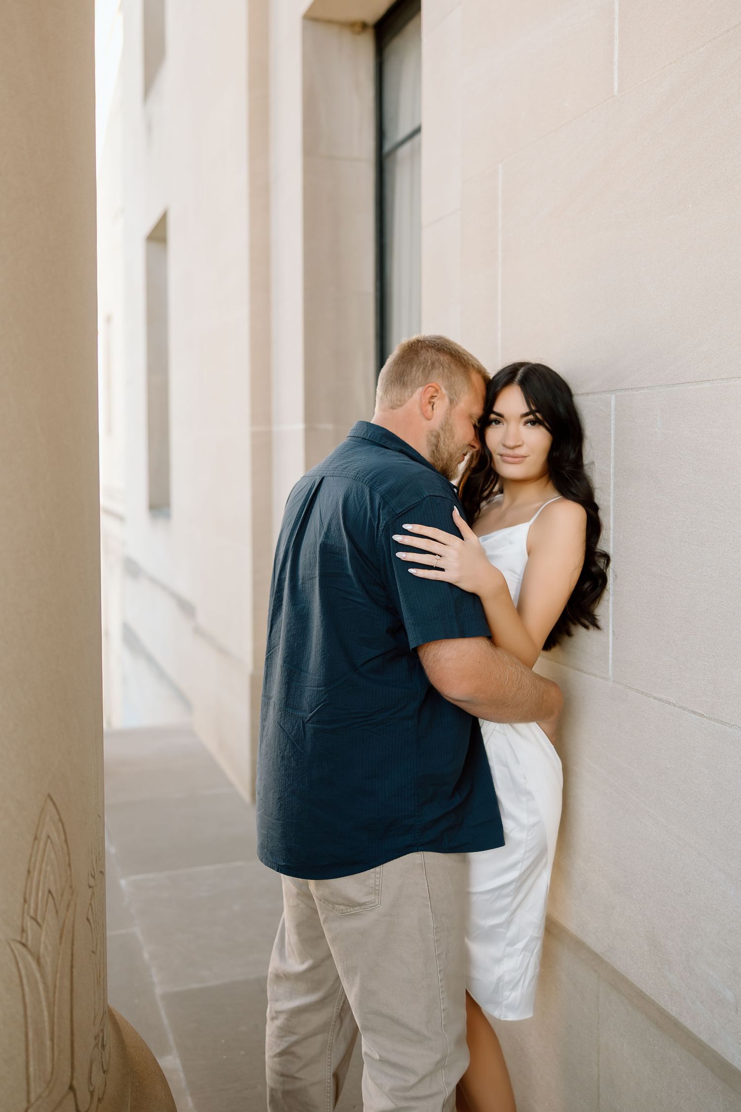 A romantic couple embraces against a white wall in a series of intimate wedding photos.