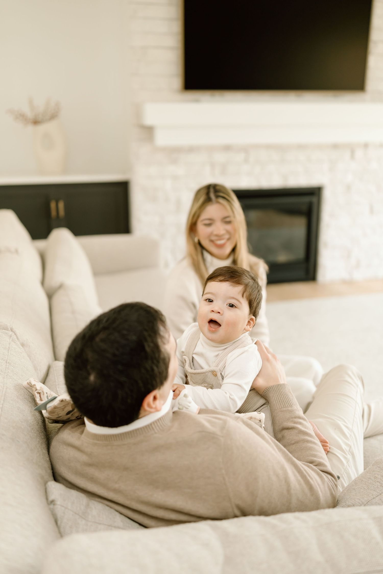 Parent and child share joyful moments while relaxing together on a white couch in a bright living room.