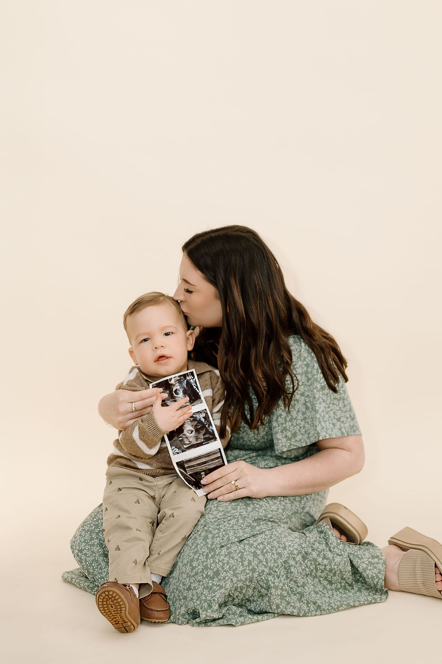A tender moment shared between parent and child while looking at ultrasound photos against a cream backdrop.