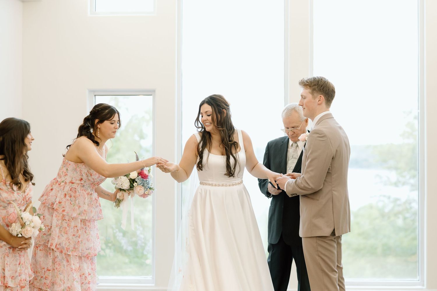 Wedding party shares joyful moment in bright indoor venue with large windows and natural lighting.