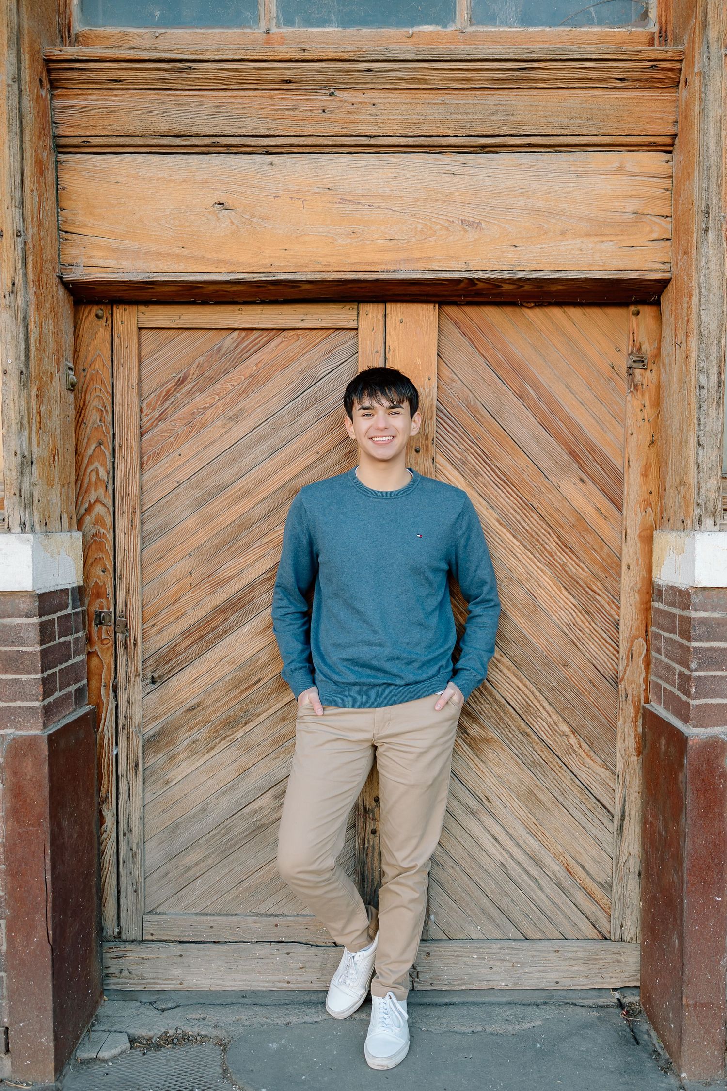 Standing pose against vintage wooden door with chevron pattern.