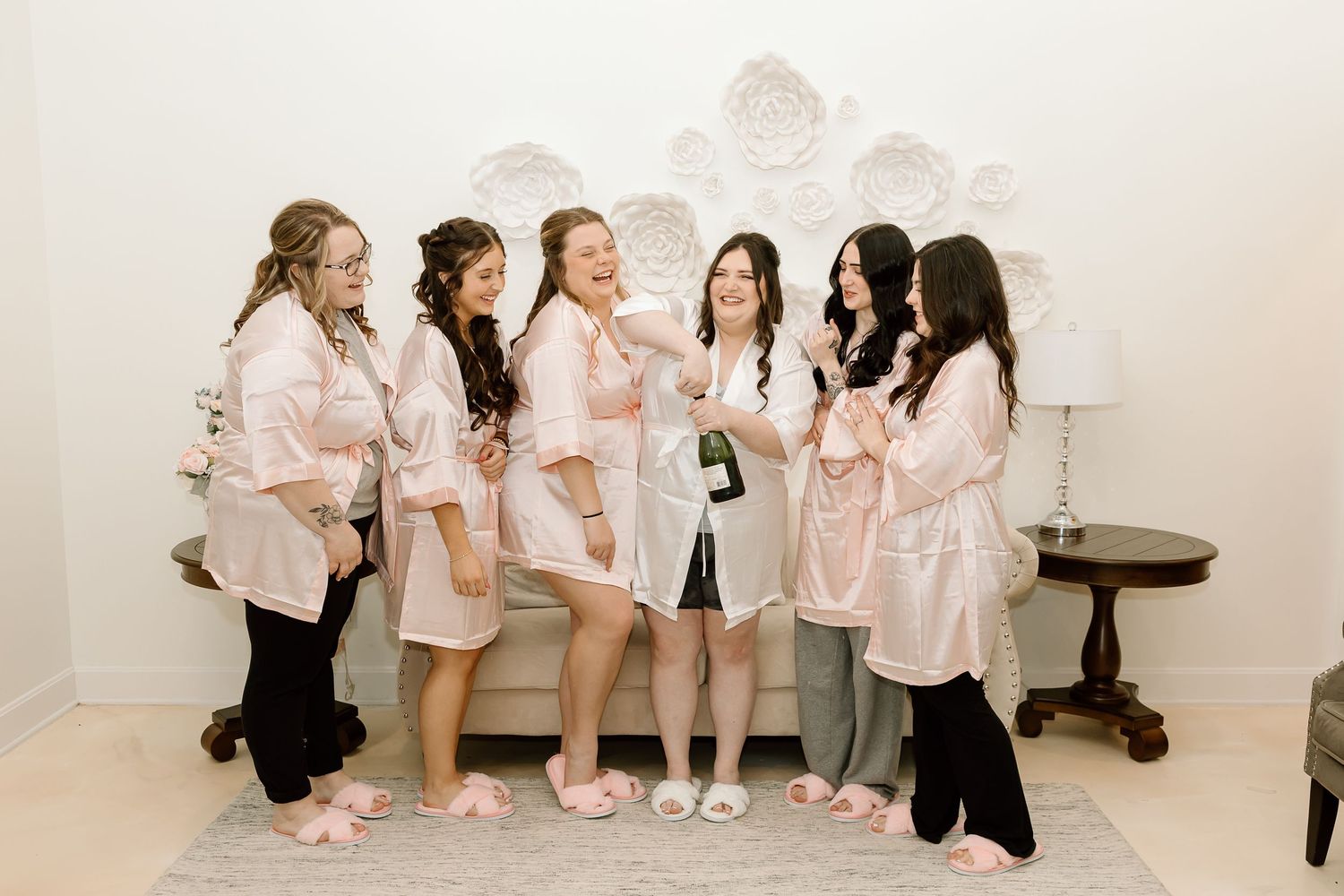 A group wearing matching white outfits poses together in a minimalist white studio space for a casual photoshoot.