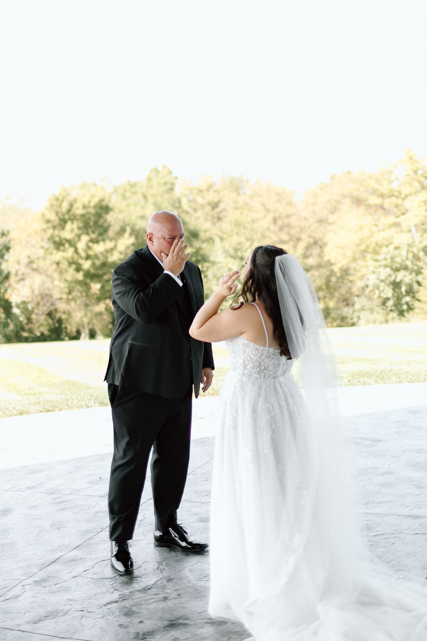 A bride and groom dance together in a series of romantic poses on a light-colored floor with trees in the background.