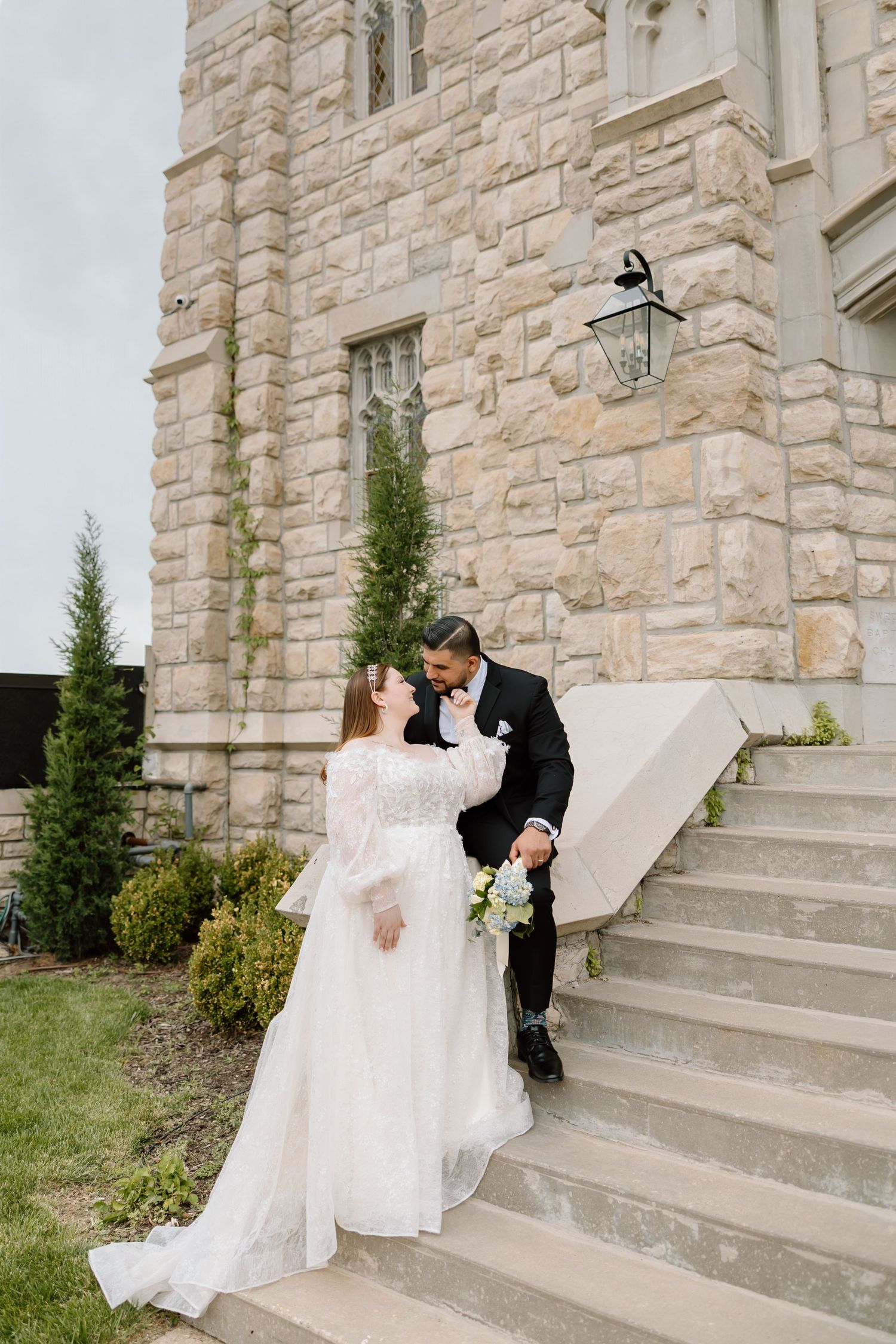 Bride and groom share a romantic moment on stone steps outside a elegant limestone church on their wedding day.