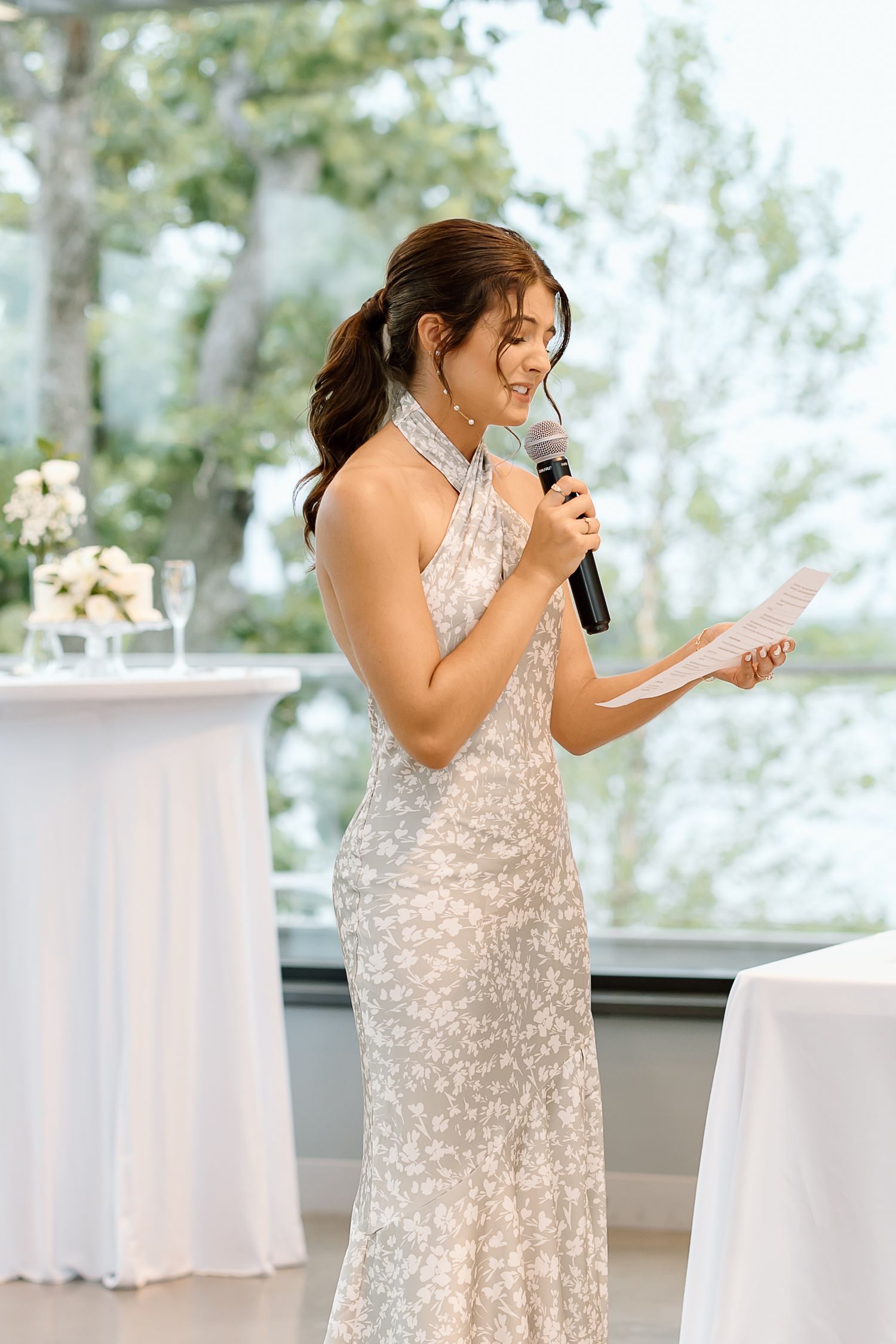 Someone in a sparkly silver gown gives a speech with a microphone at an elegant wedding reception.