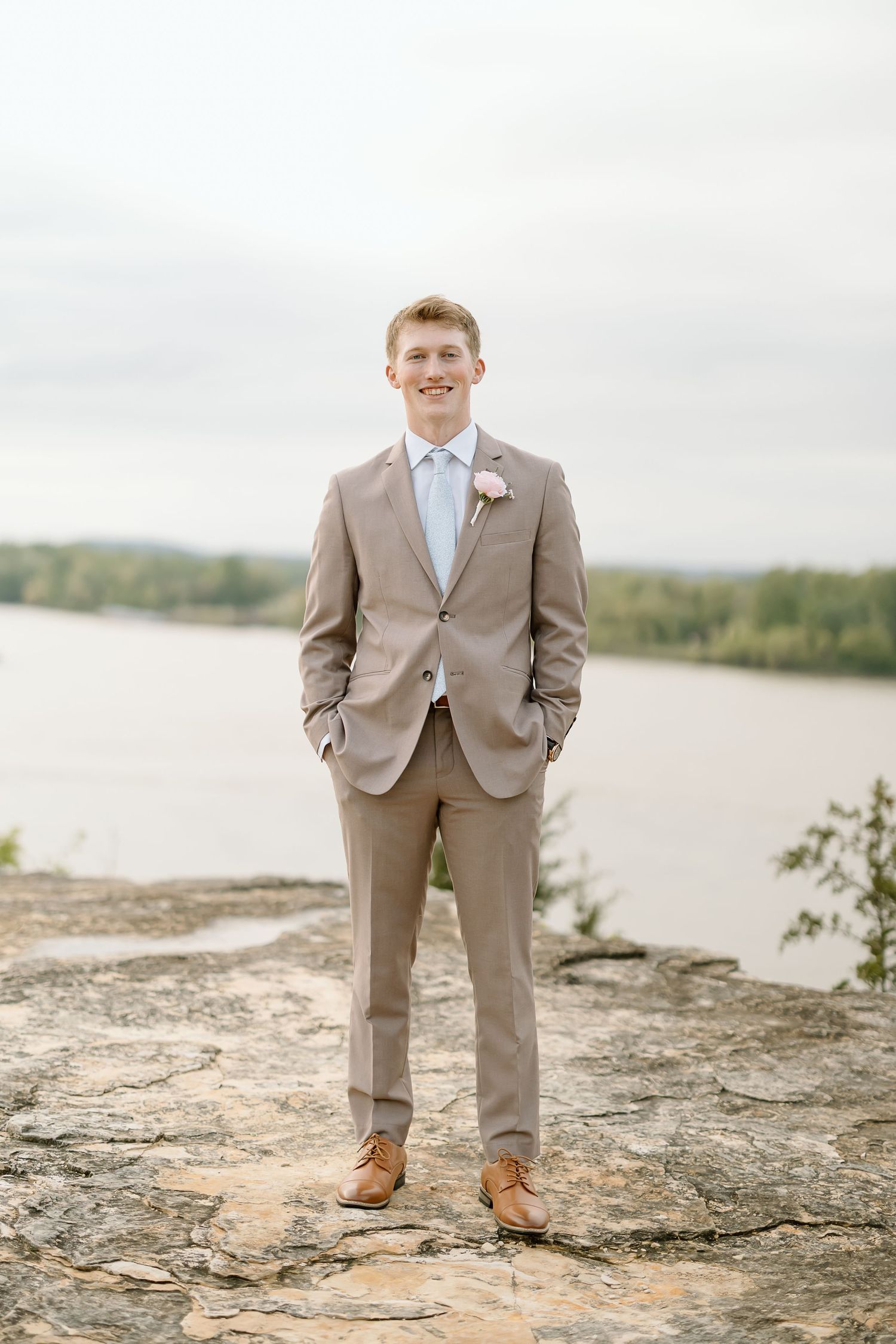 Three photos of a person in a tan suit and blue tie standing on rocky terrain near a waterfront.