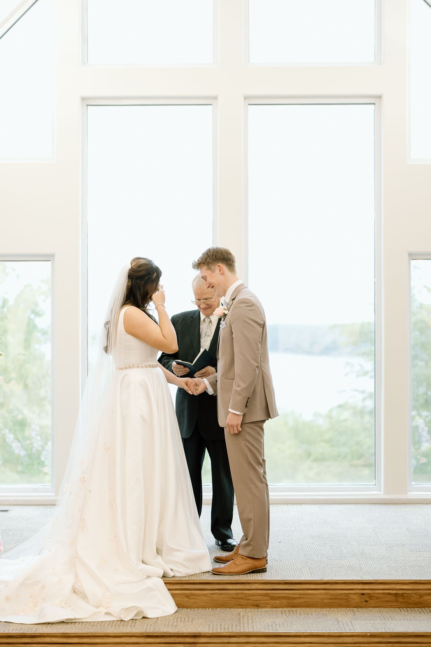 A couple shares an intimate moment during their first look at a bright indoor venue with large windows.