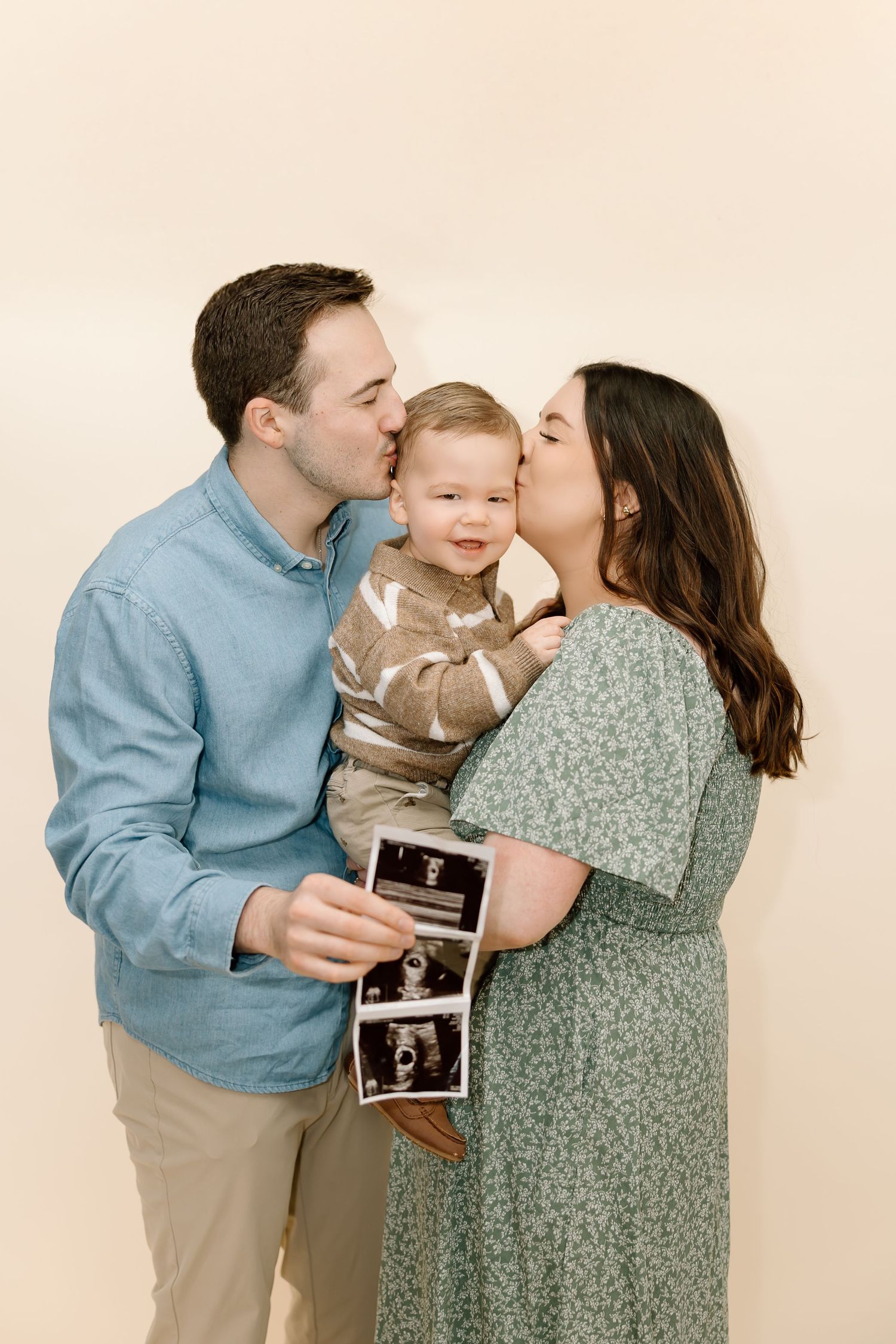A family shares loving kisses and holds an ultrasound photo in a series of heartwarming pregnancy announcement portraits.