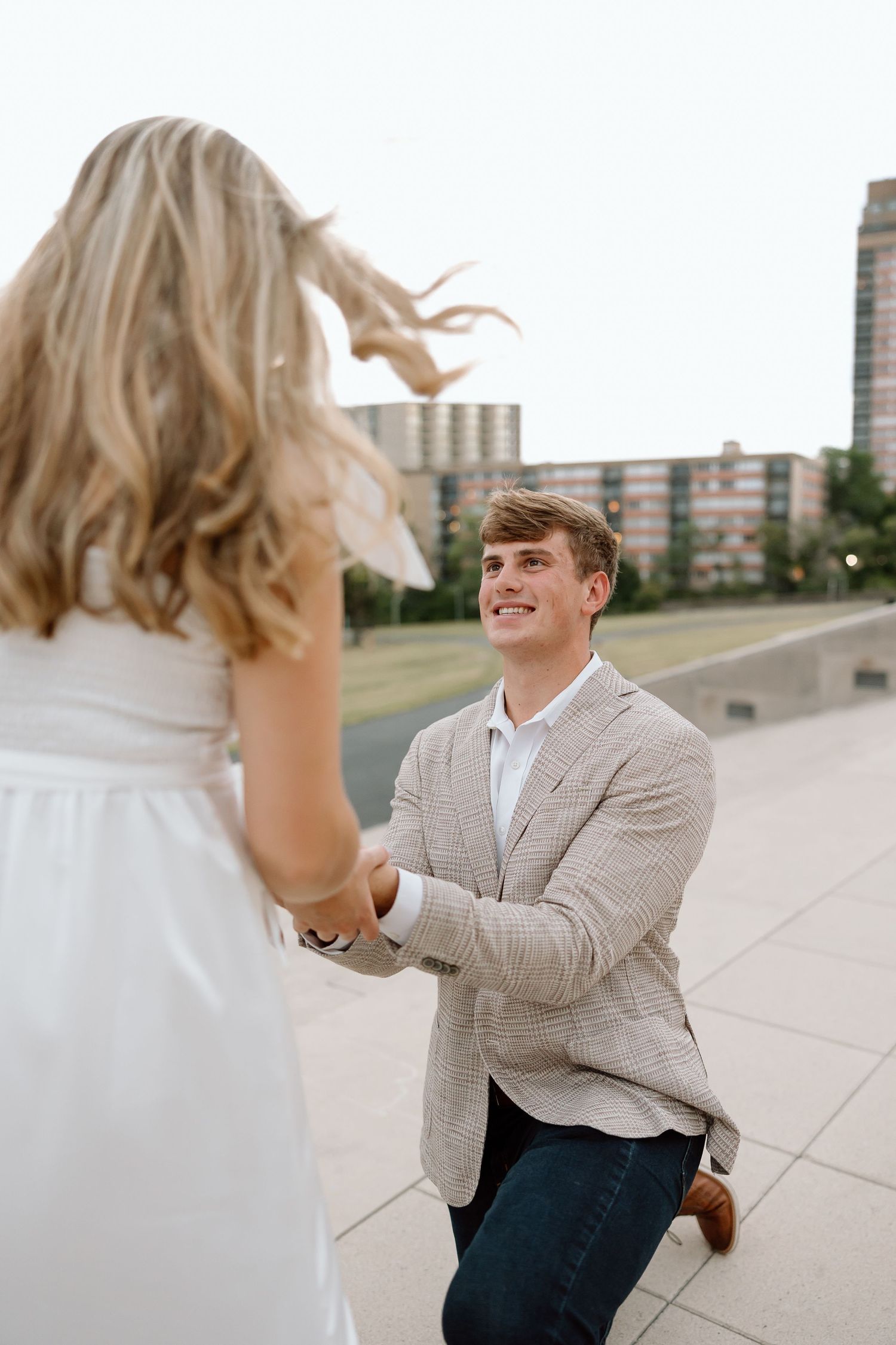A couple shares a romantic moment during a proposal on a city rooftop with urban buildings in the background.