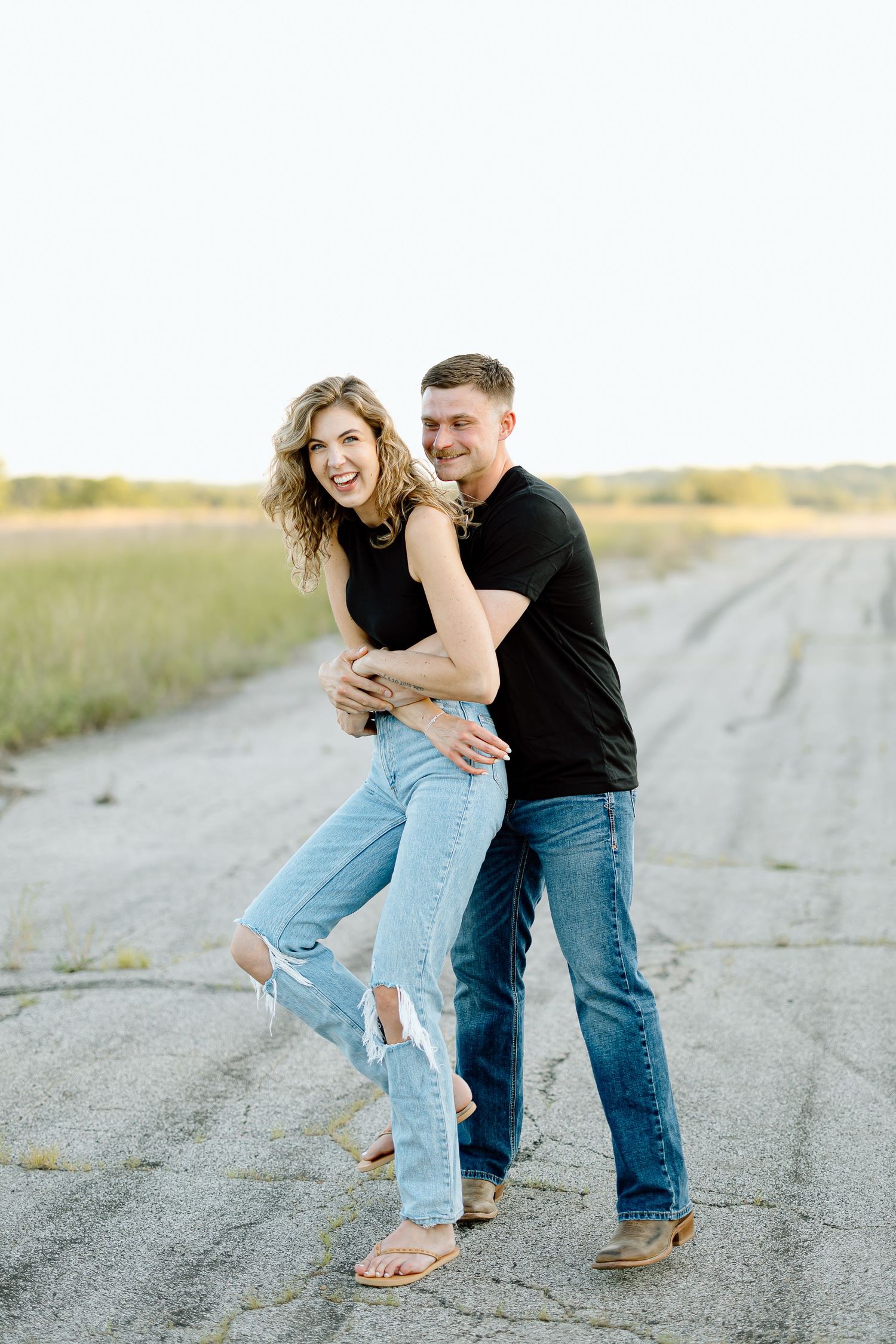 A couple playfully poses together on a dirt road during a casual outdoor photo session.