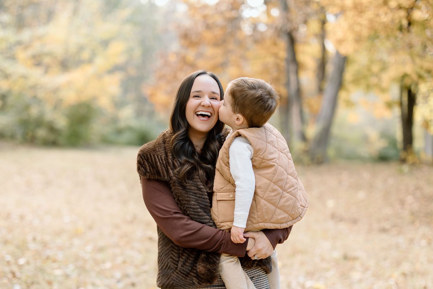 Parent and child share tender moments while playing in autumn leaves during a golden sunset photo session.