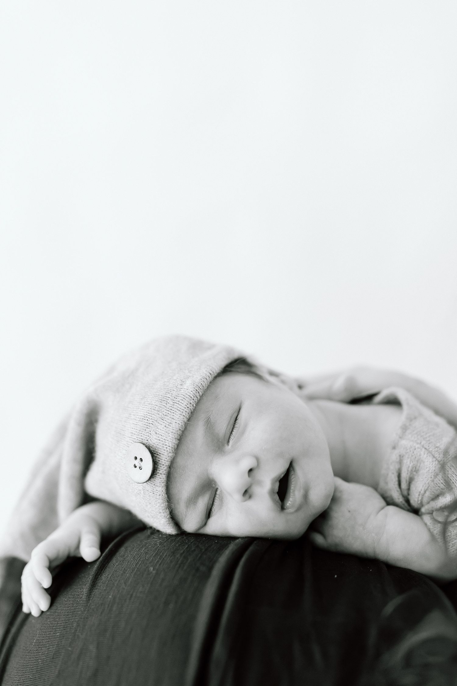A peaceful black and white portrait of a sleeping baby resting on dark fabric.