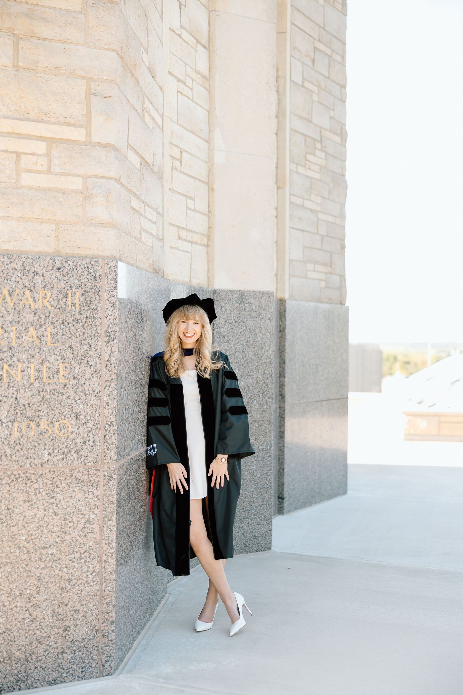 A person in a black jacket and beanie poses against a stone wall in an urban setting.