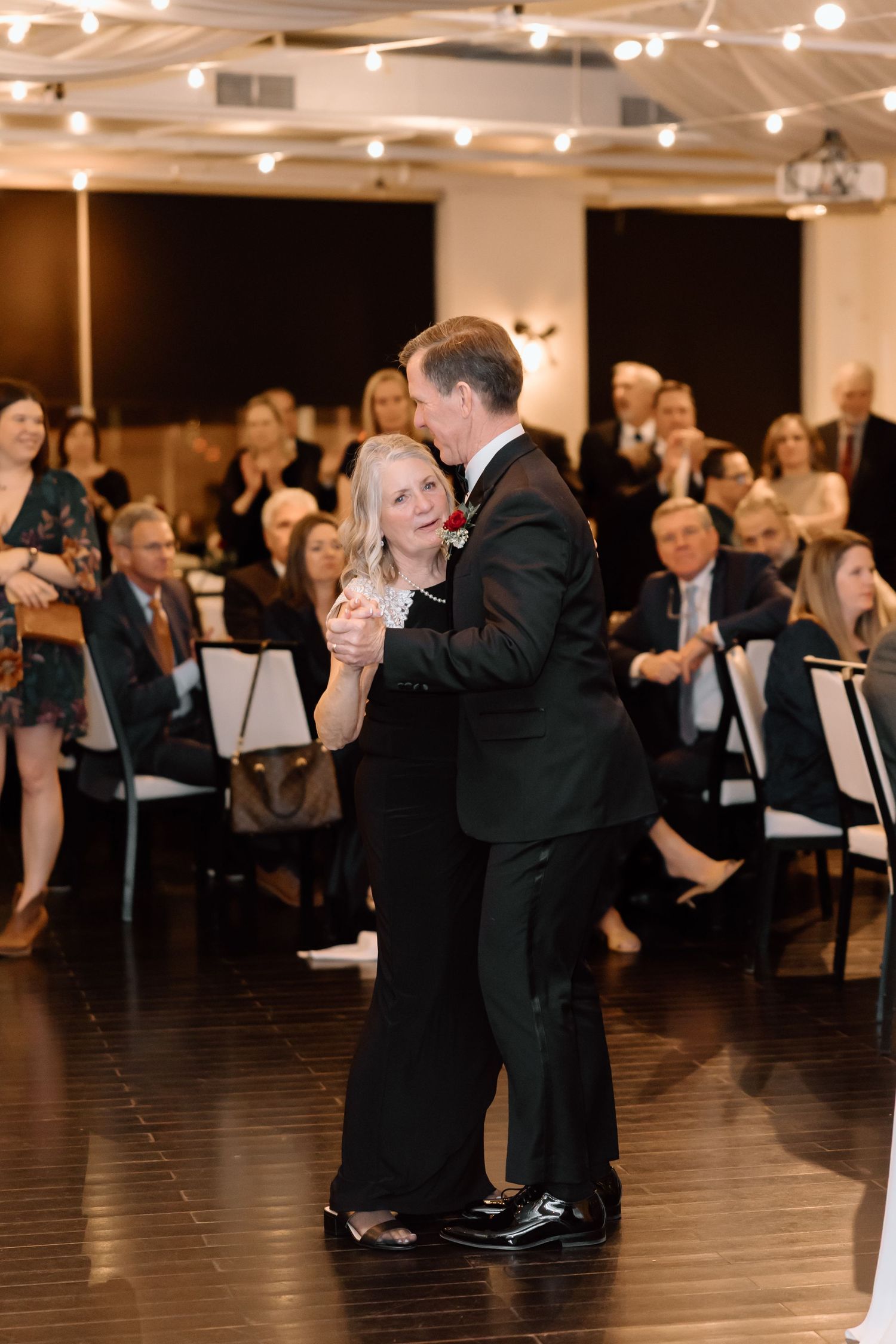 Couples dancing together at an elegant evening reception with string lights overhead and dark flooring.
