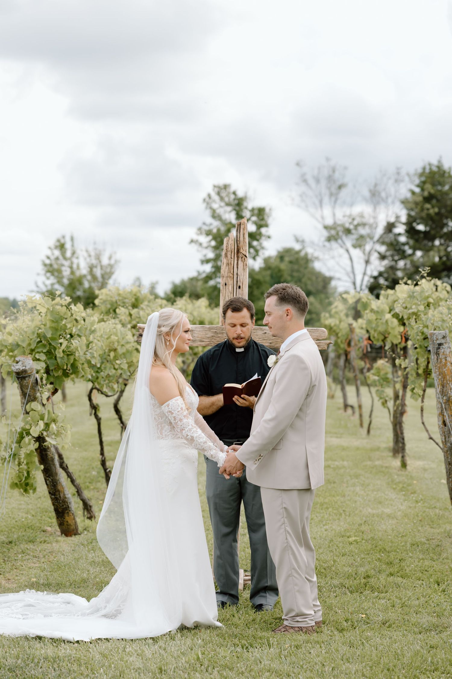 Bride and groom exchange vows outdoors in a vineyard wedding ceremony with an officiant holding a book.