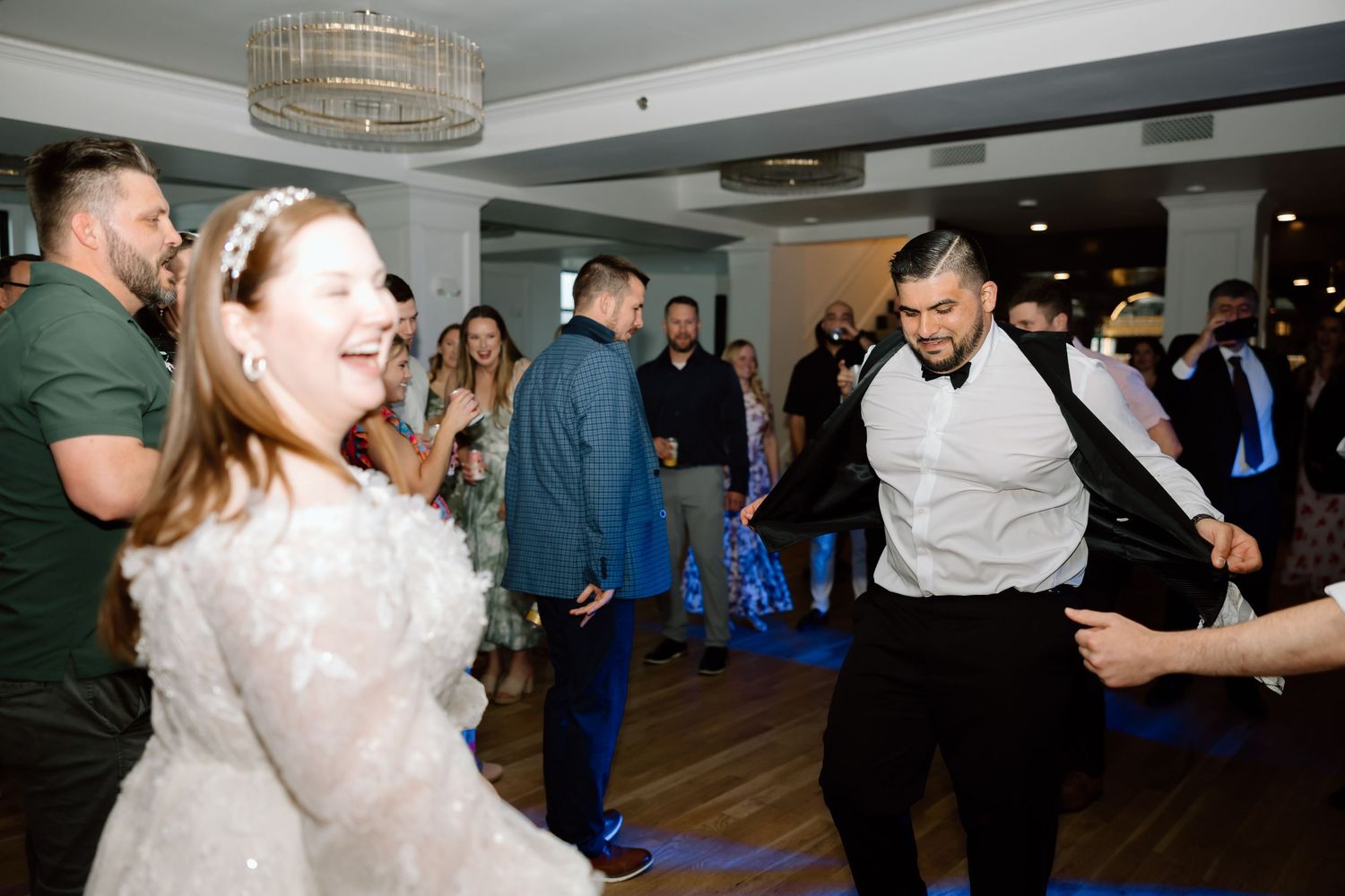 Bride and groom dancing joyfully with guests at a wedding reception in an elegant venue.